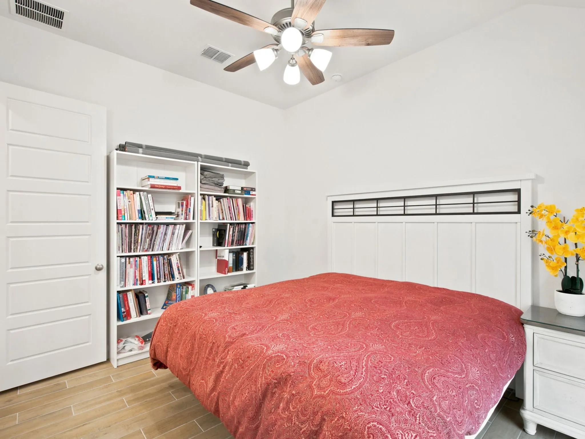 Vaulted ceiling with a ceiling fan, white paneled door, wood-finish flooring, and white built-in shelving