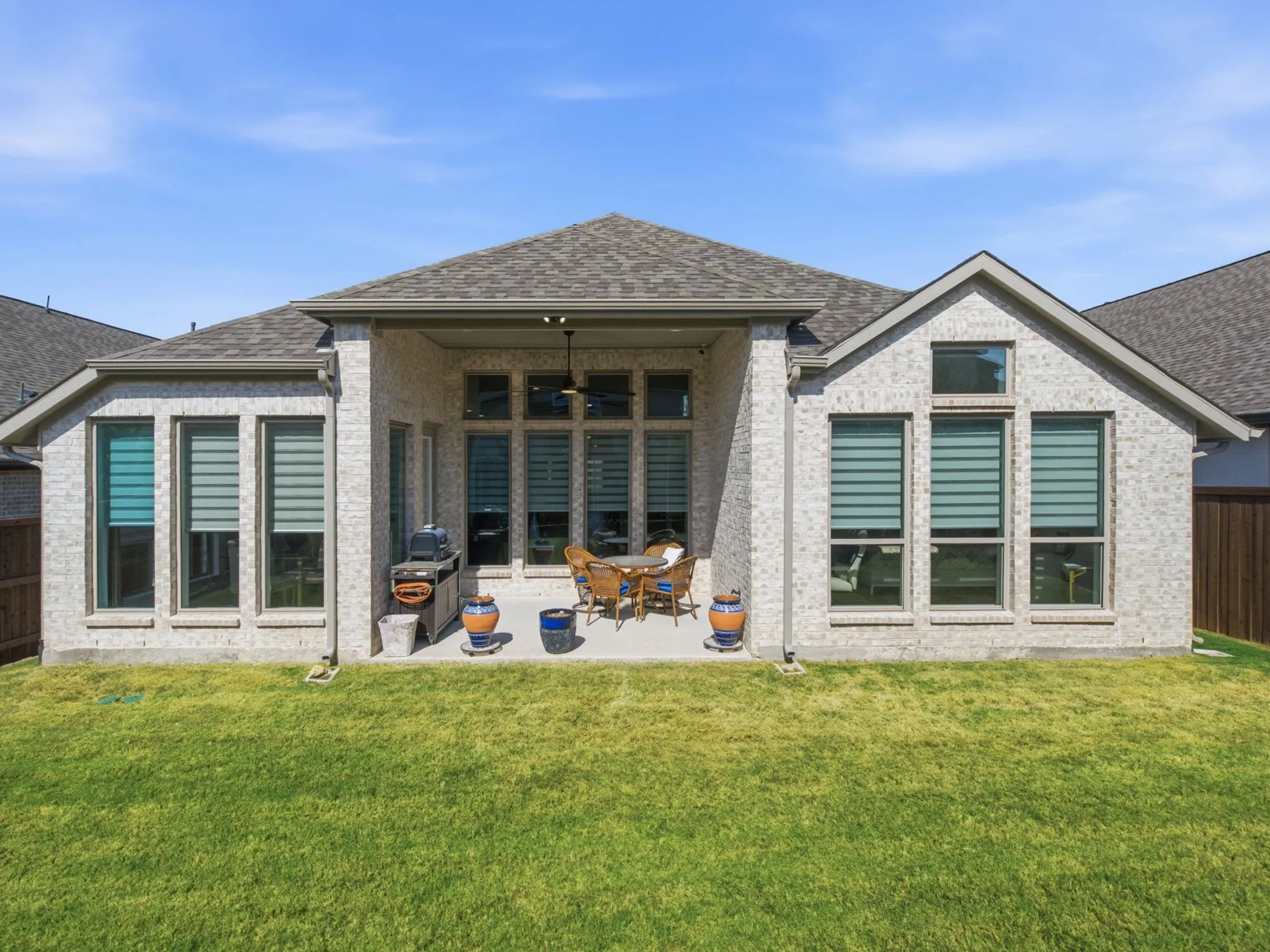 Brick exterior with multiple large windows, covered patio, outdoor ceiling fan, and a spacious green lawn