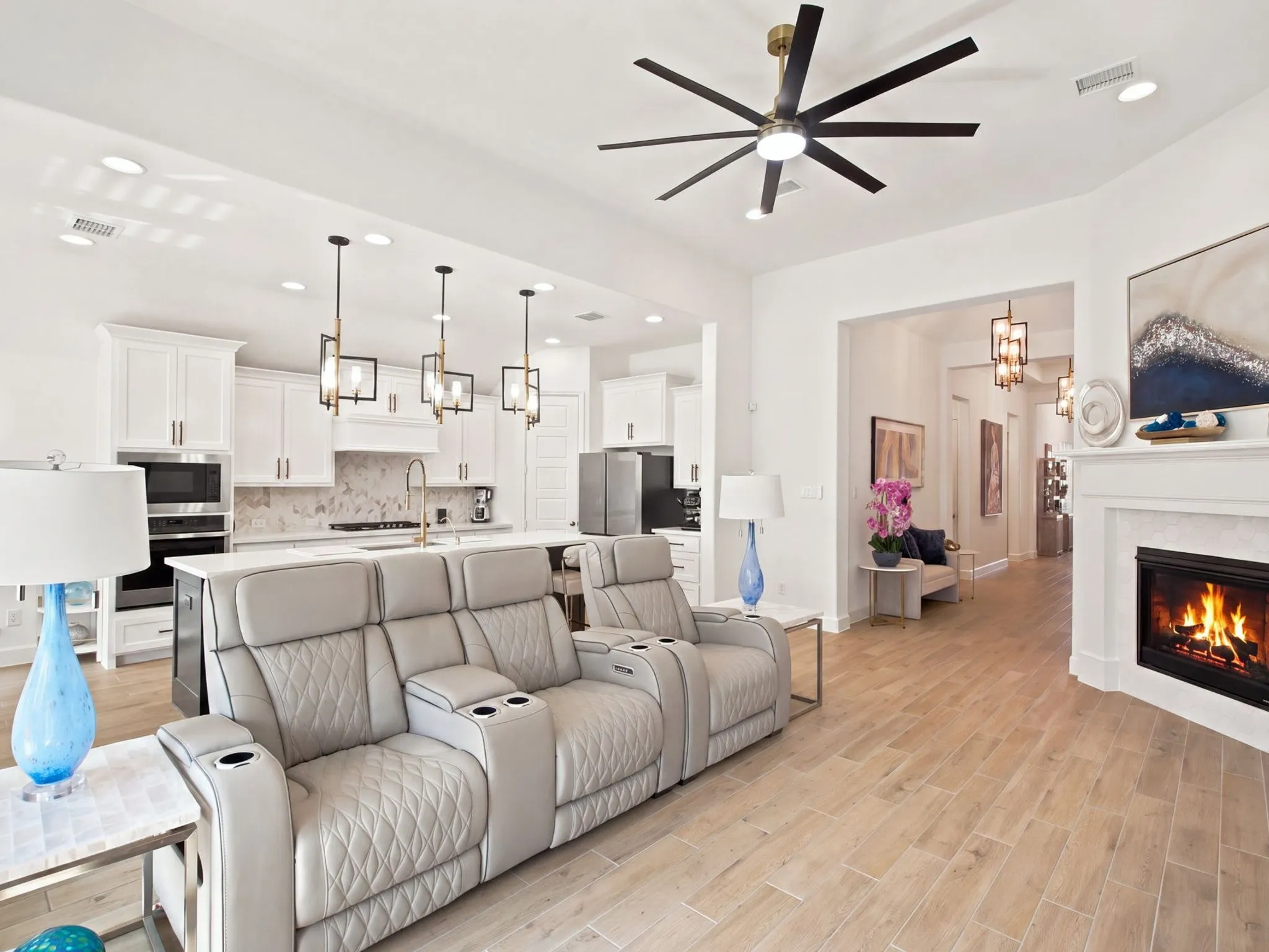 Open-concept living area featuring wood-finish flooring, a contemporary fireplace with a white mantel, and a modern ceiling fan