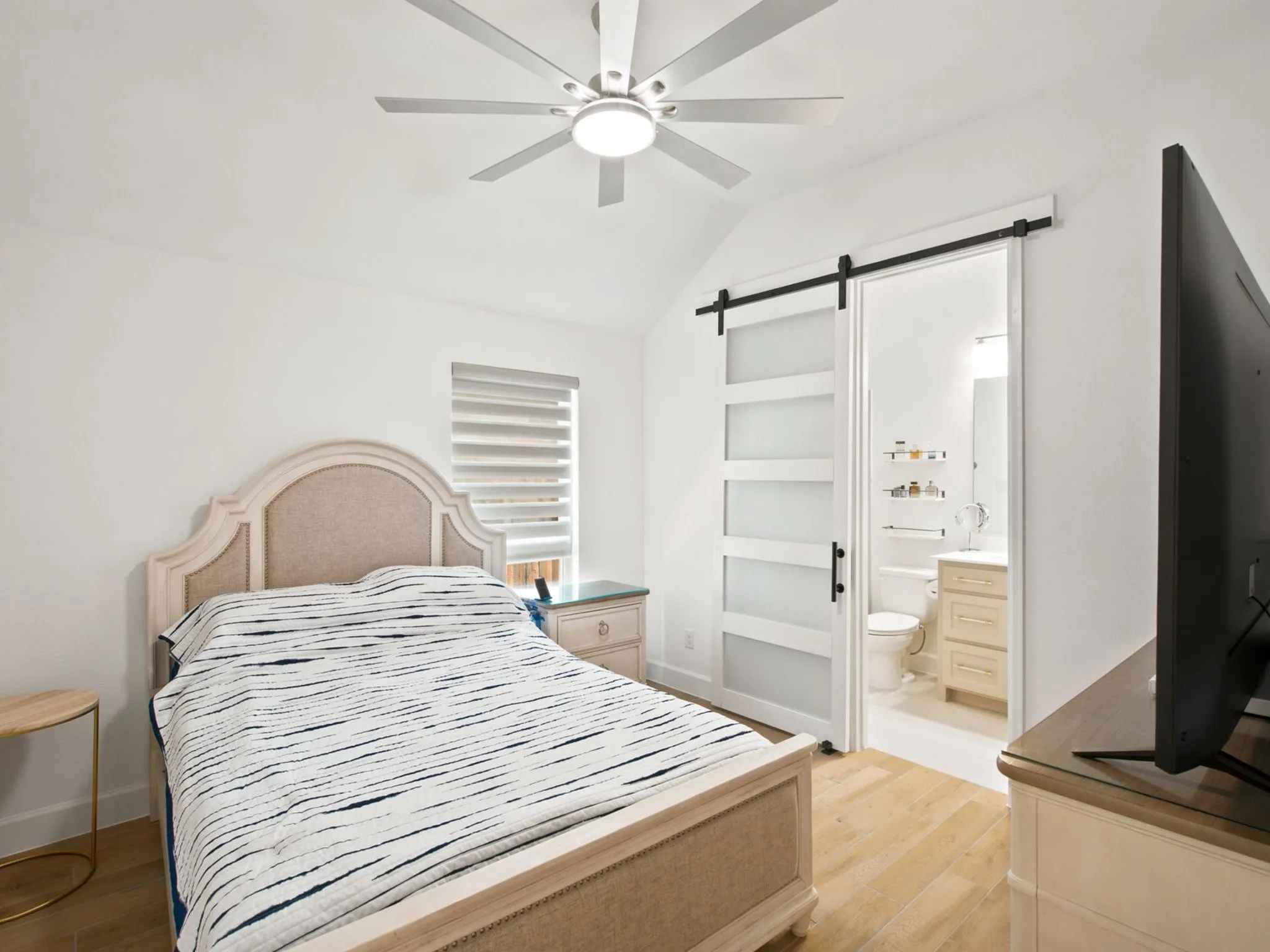 Vaulted ceiling with an integrated ceiling fan, wood-finish flooring, and a modern sliding barn door with frosted panels