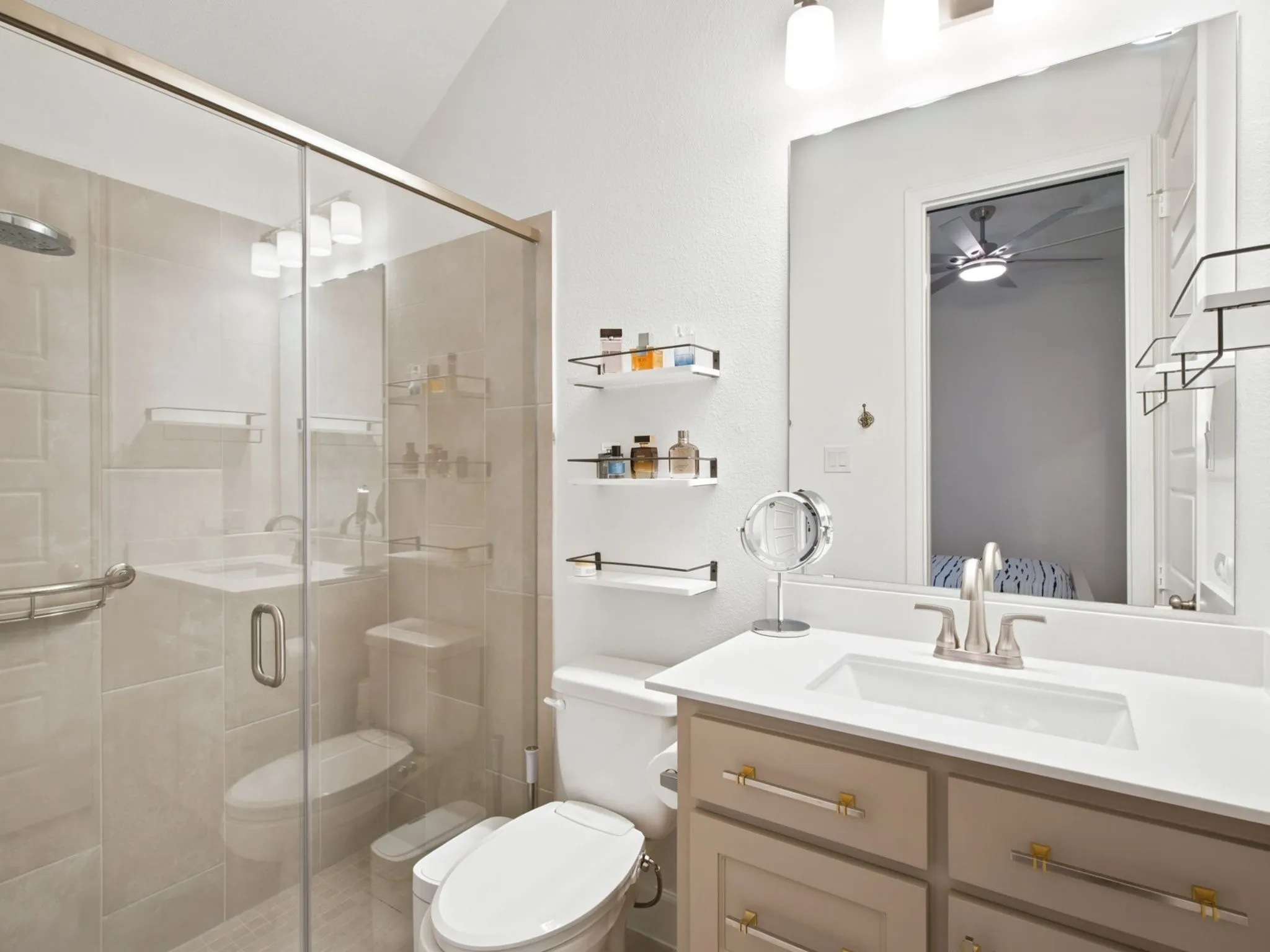 Glass-enclosed shower with tile surround and integrated shelving, vanity with integrated sink and chrome fixtures, frameless mirror, and vaulted ceiling