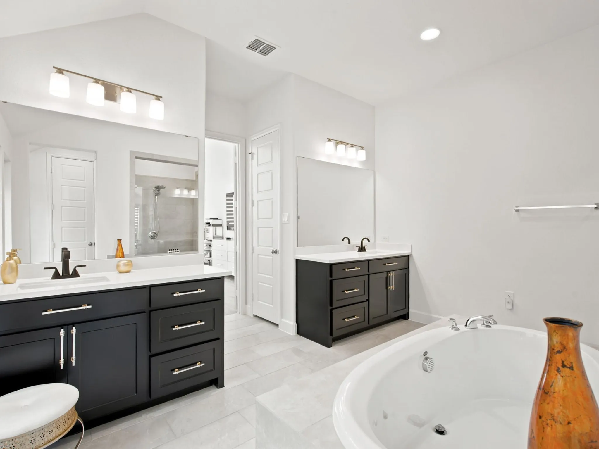 Dual vanities with dark cabinetry and white countertops, large soaking tub, and tiled flooring