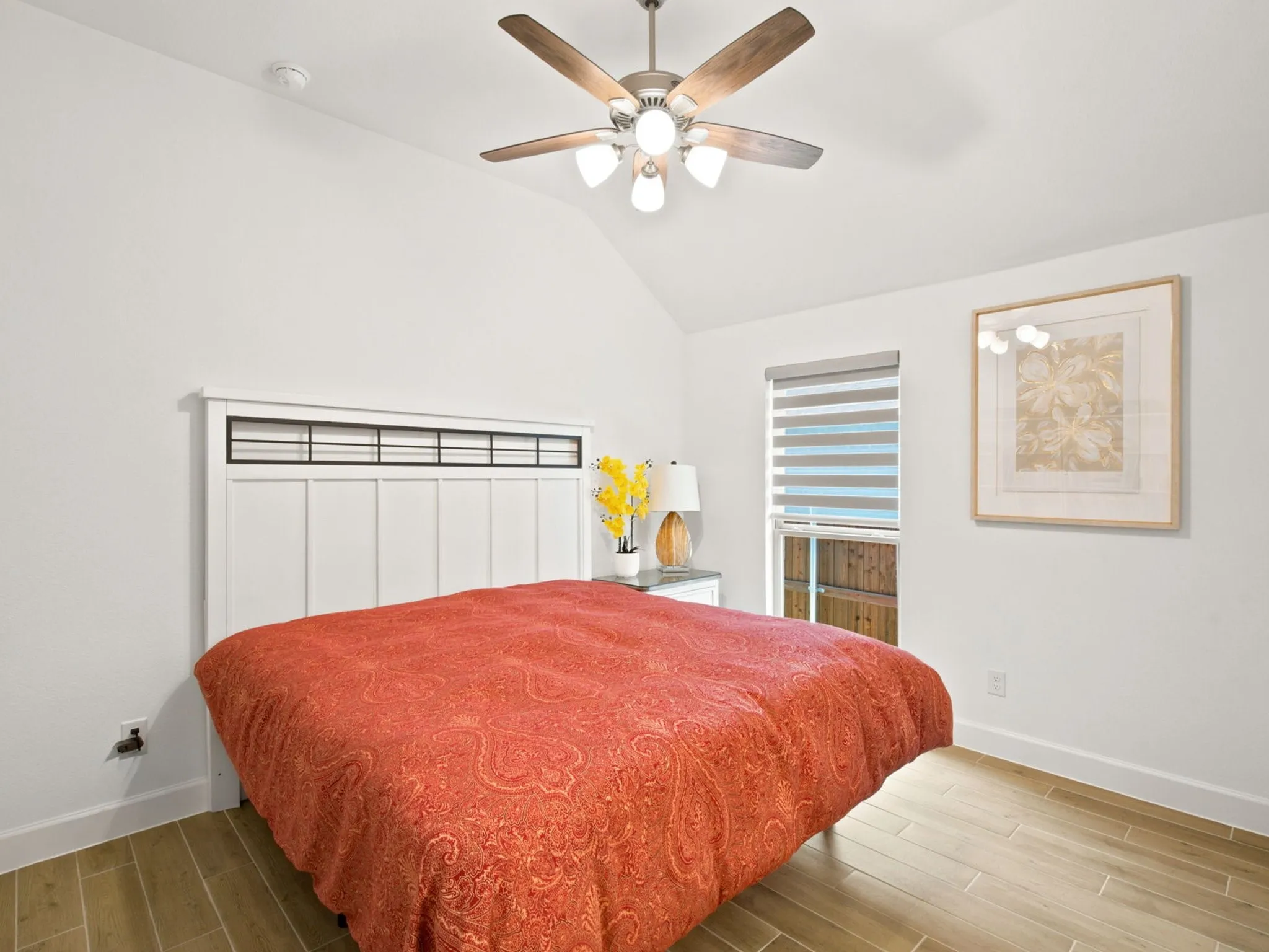 Vaulted ceiling with a ceiling fan and light fixture, wood-finish flooring, and a large window with privacy blinds