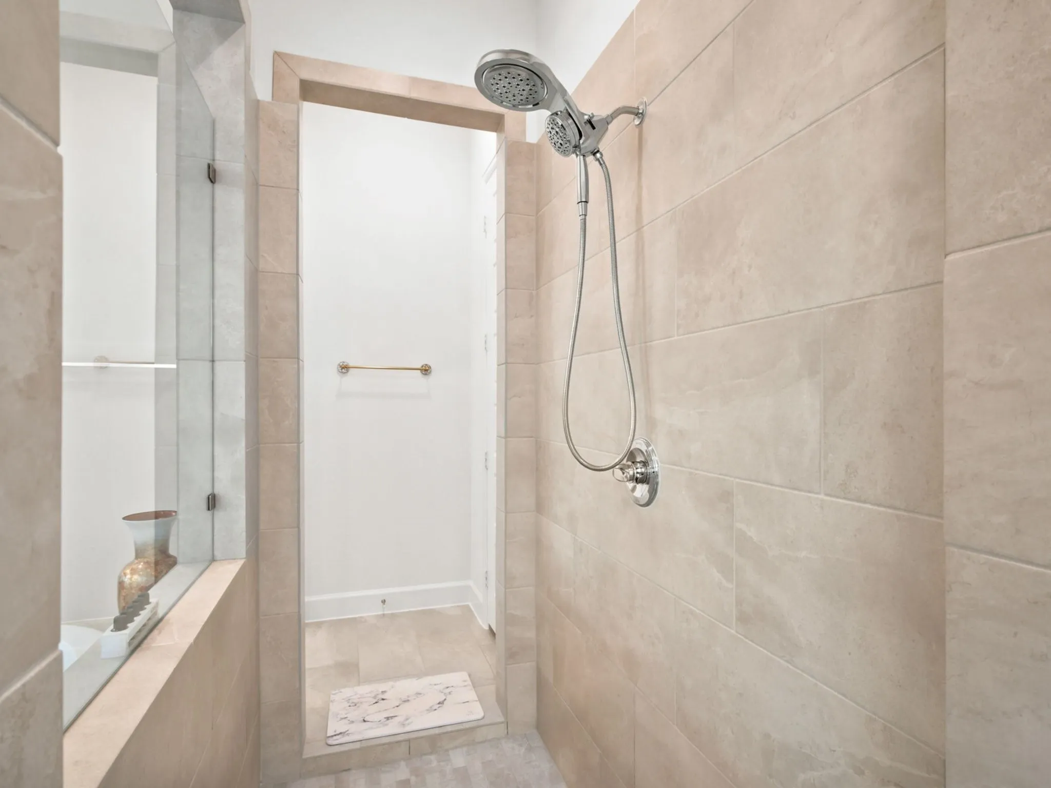 Tiled shower enclosure featuring a multi-function showerhead, polished chrome fixtures, and a glass partition