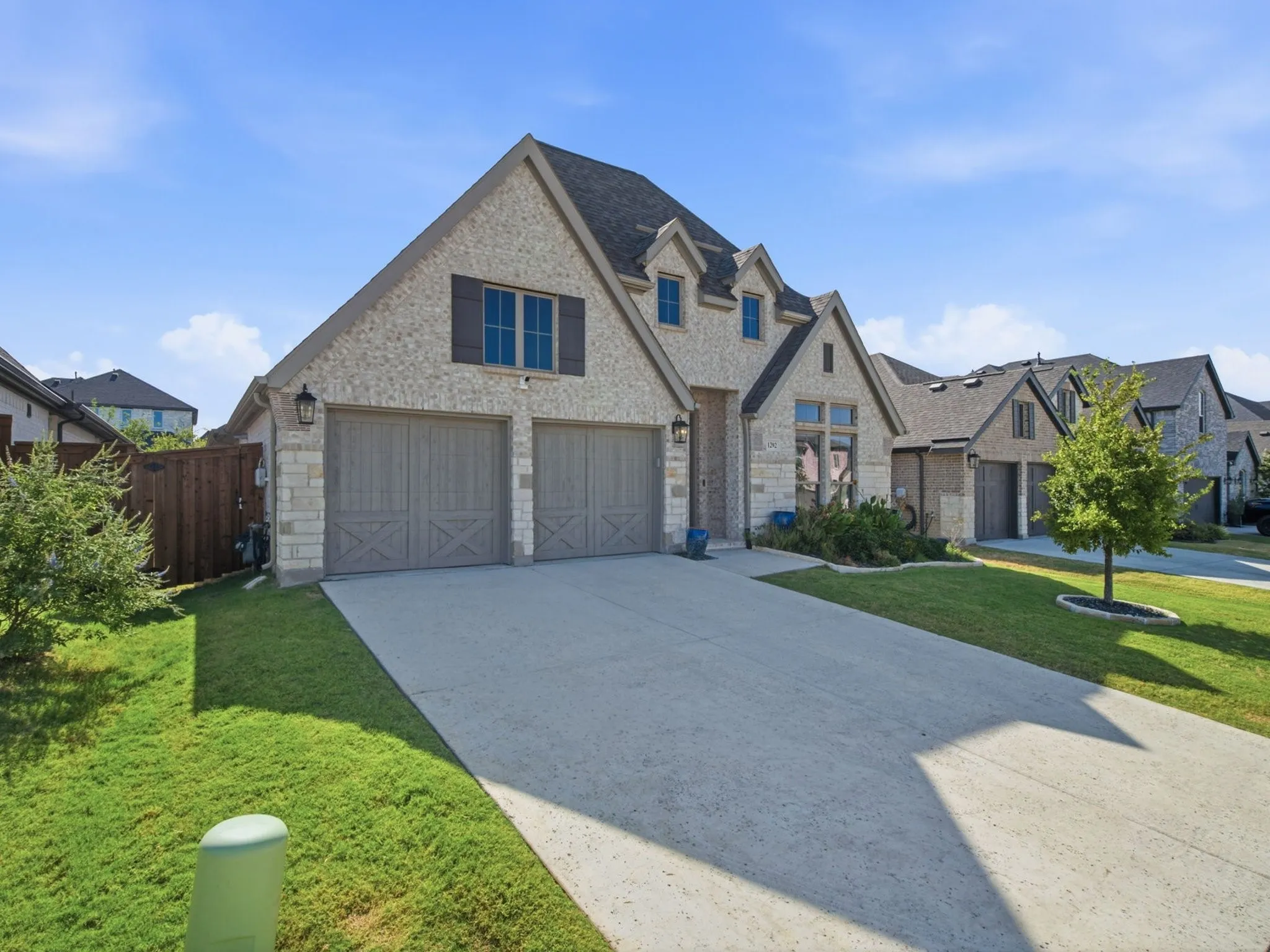 Stone and brick exterior with a two-car garage, dormer windows, and a concrete driveway