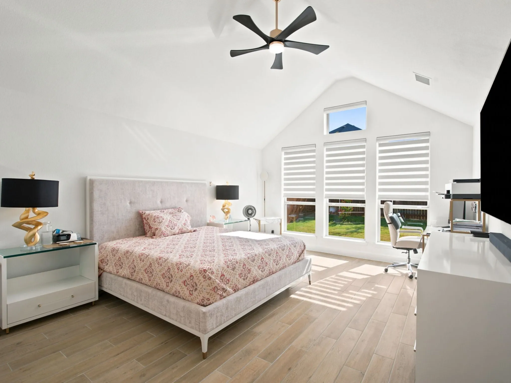 Vaulted ceiling, modern ceiling fan, three large windows with blinds, wood-finish flooring, and additional window above
