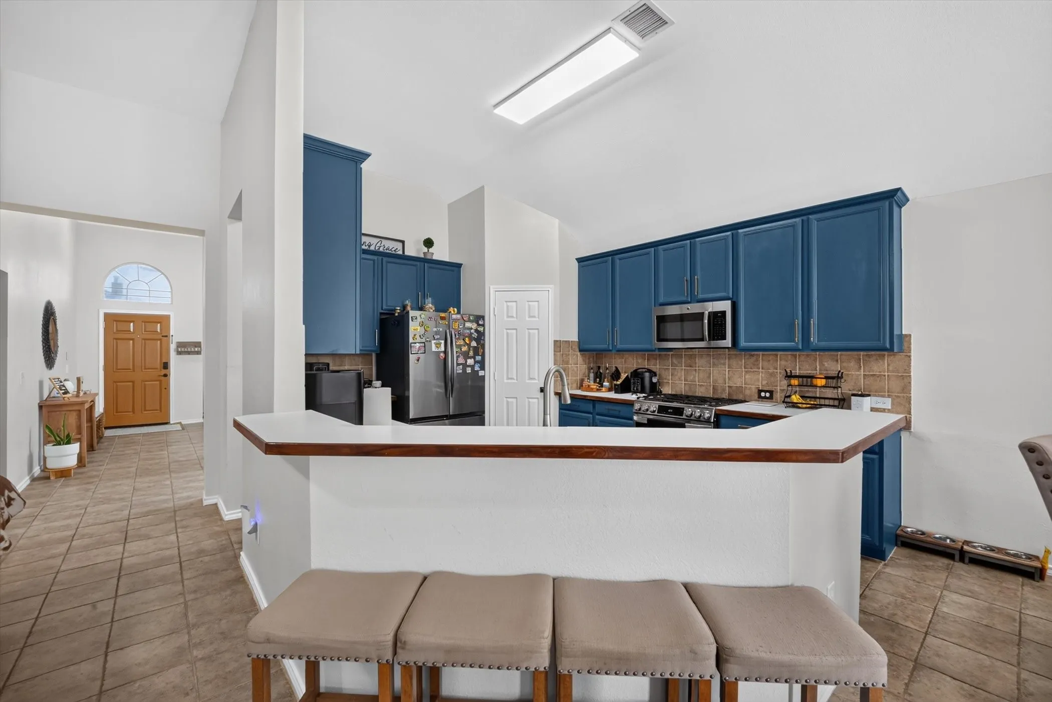 Kitchen featuring blue cabinetry, a stainless steel microwave, and tile backsplash
