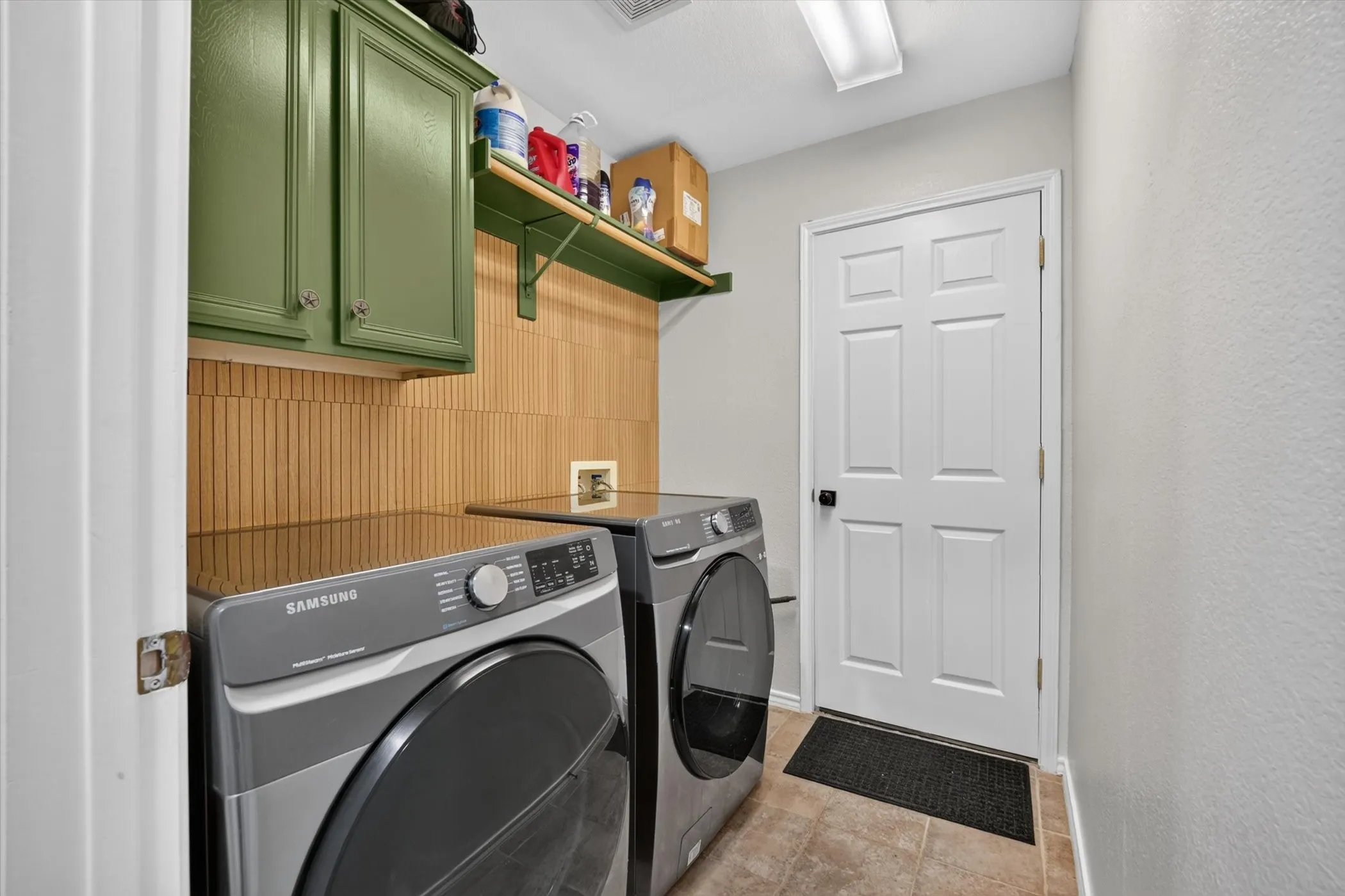 Laundry area featuring green cabinetry, wood-finish wall paneling, and tile flooring