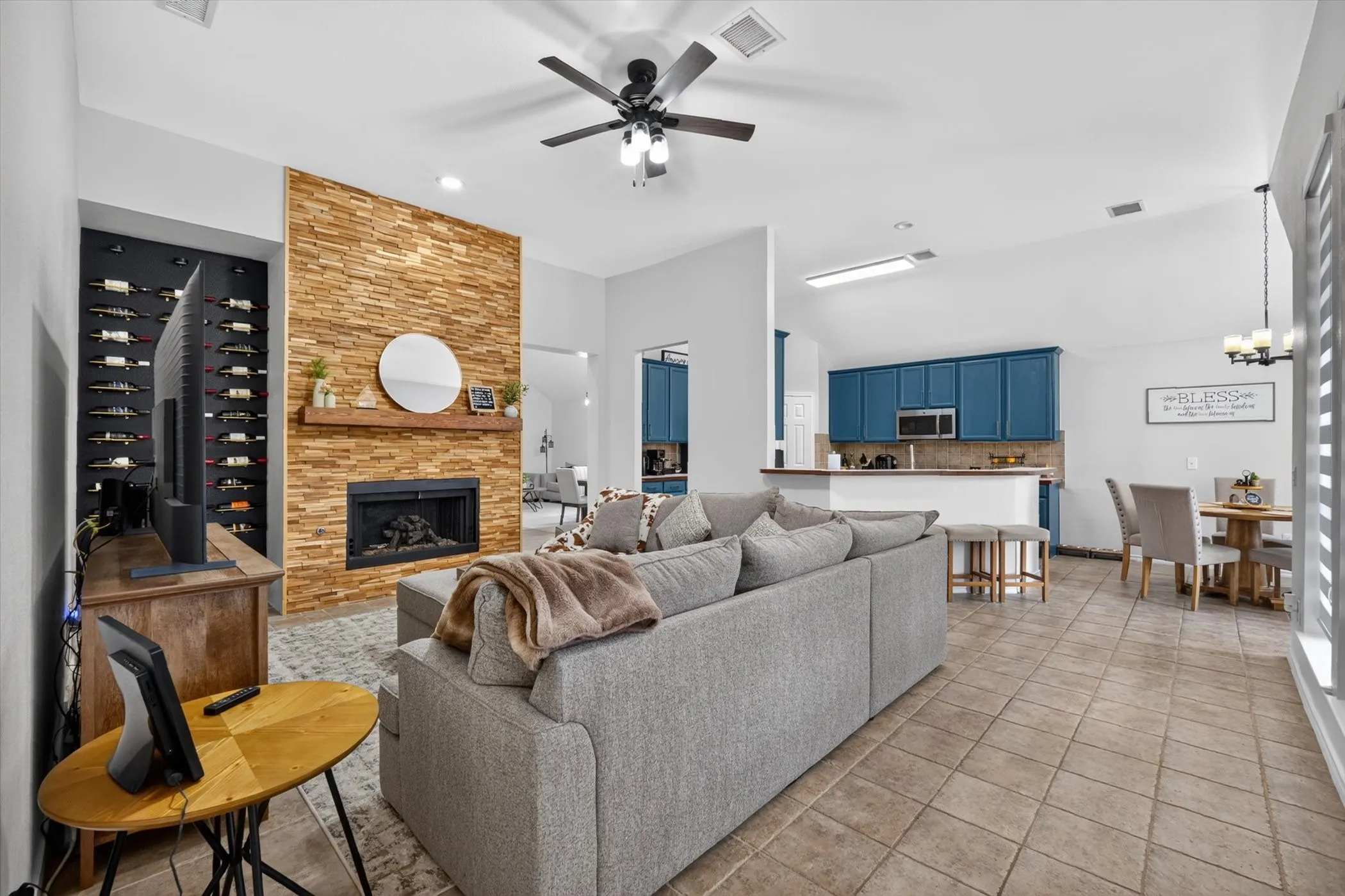 Open-concept living space featuring a stacked stone fireplace with a wood mantle, a built-in recessed wine rack, and a ceiling fan