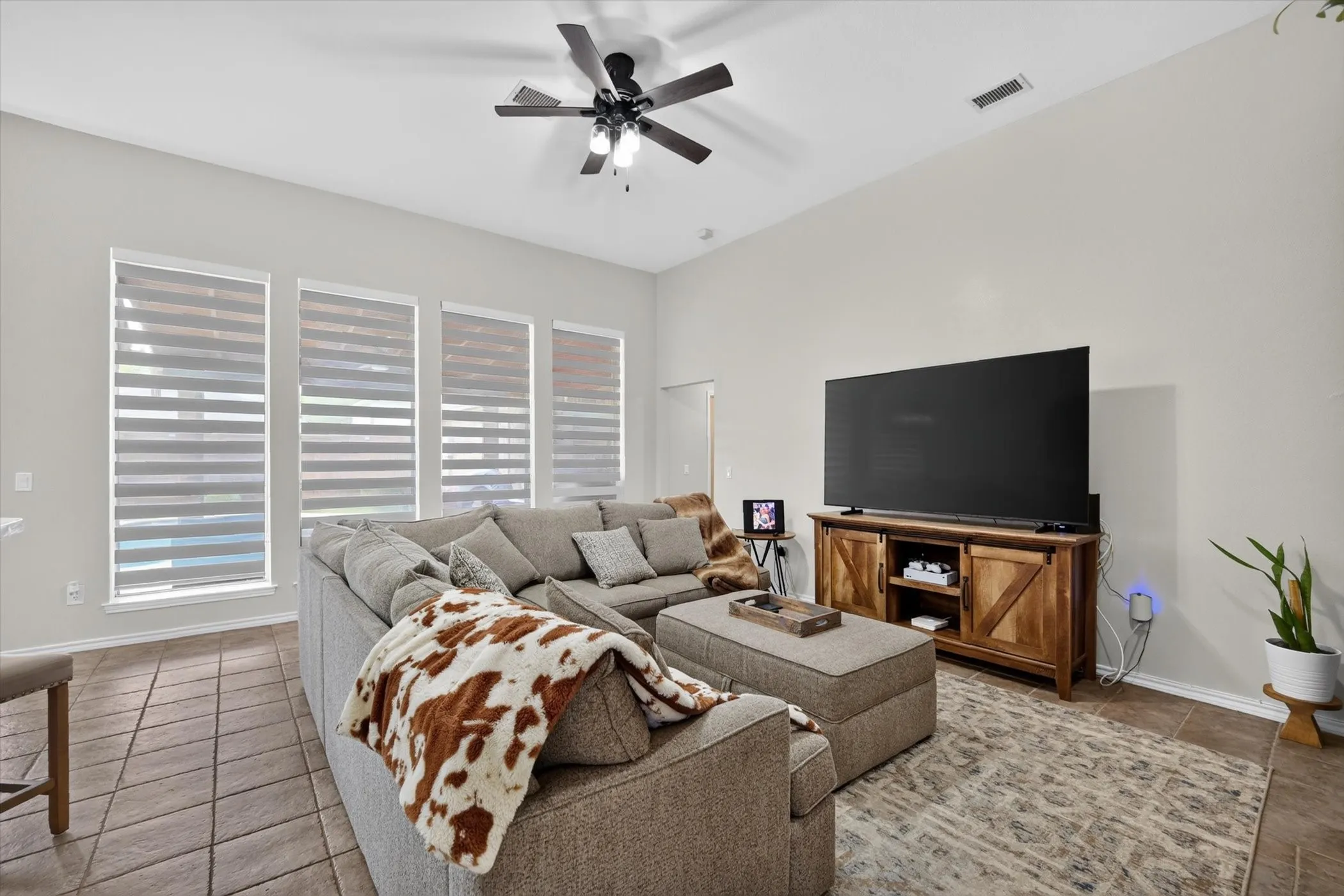 Living area featuring high ceilings, a ceiling fan with integrated lighting, four tall windows with horizontal blinds, and tile flooring