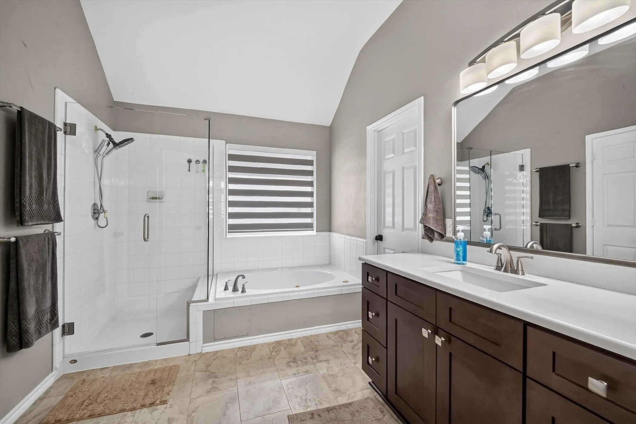 Spacious bathroom featuring a glass-enclosed shower with white subway tile, a built-in soaking tub, and a dark wood-finish vanity with a white countertop and rectangular sink