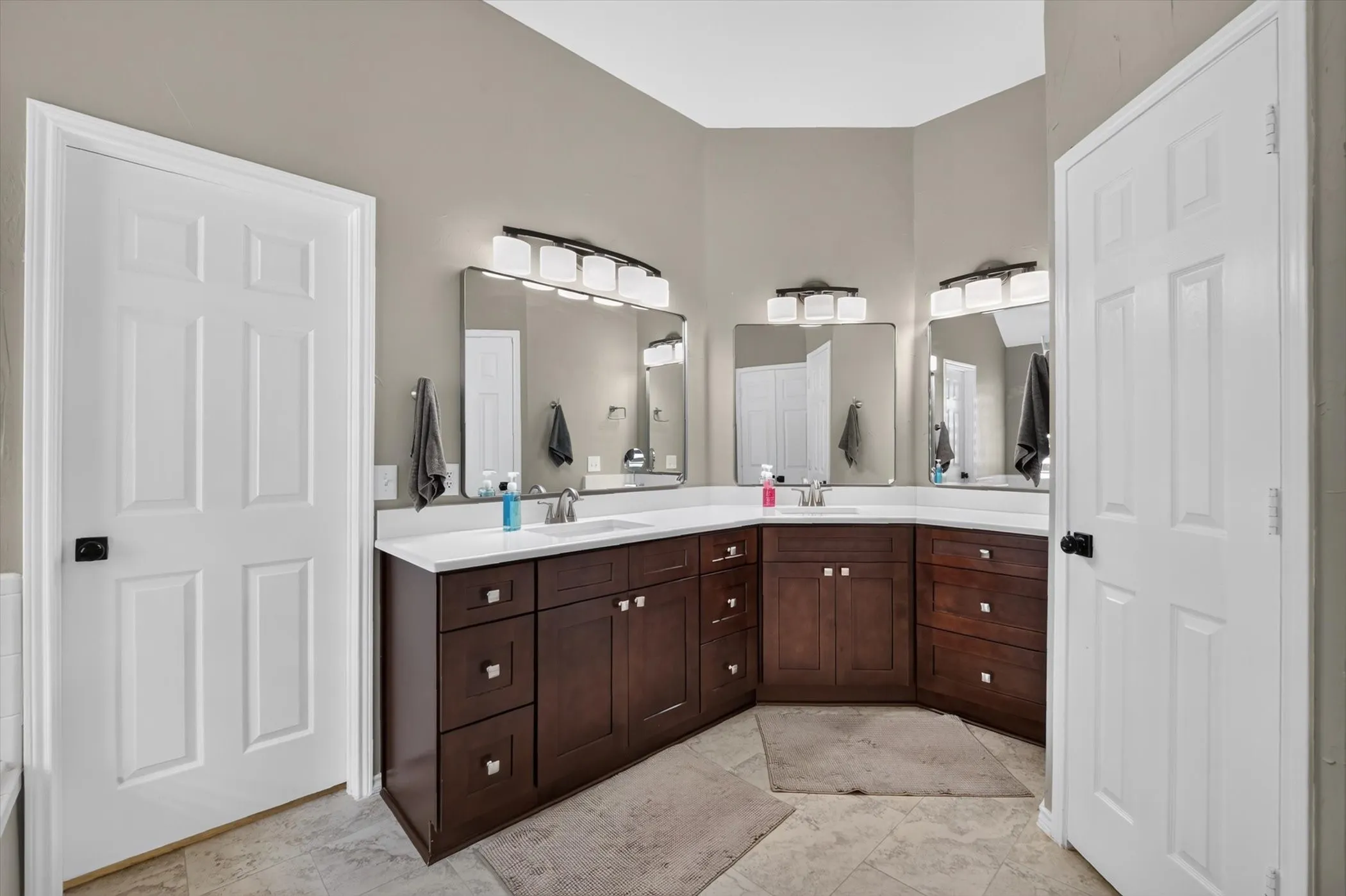 Dual vanities with wood cabinetry, white countertops, and individual mirrors