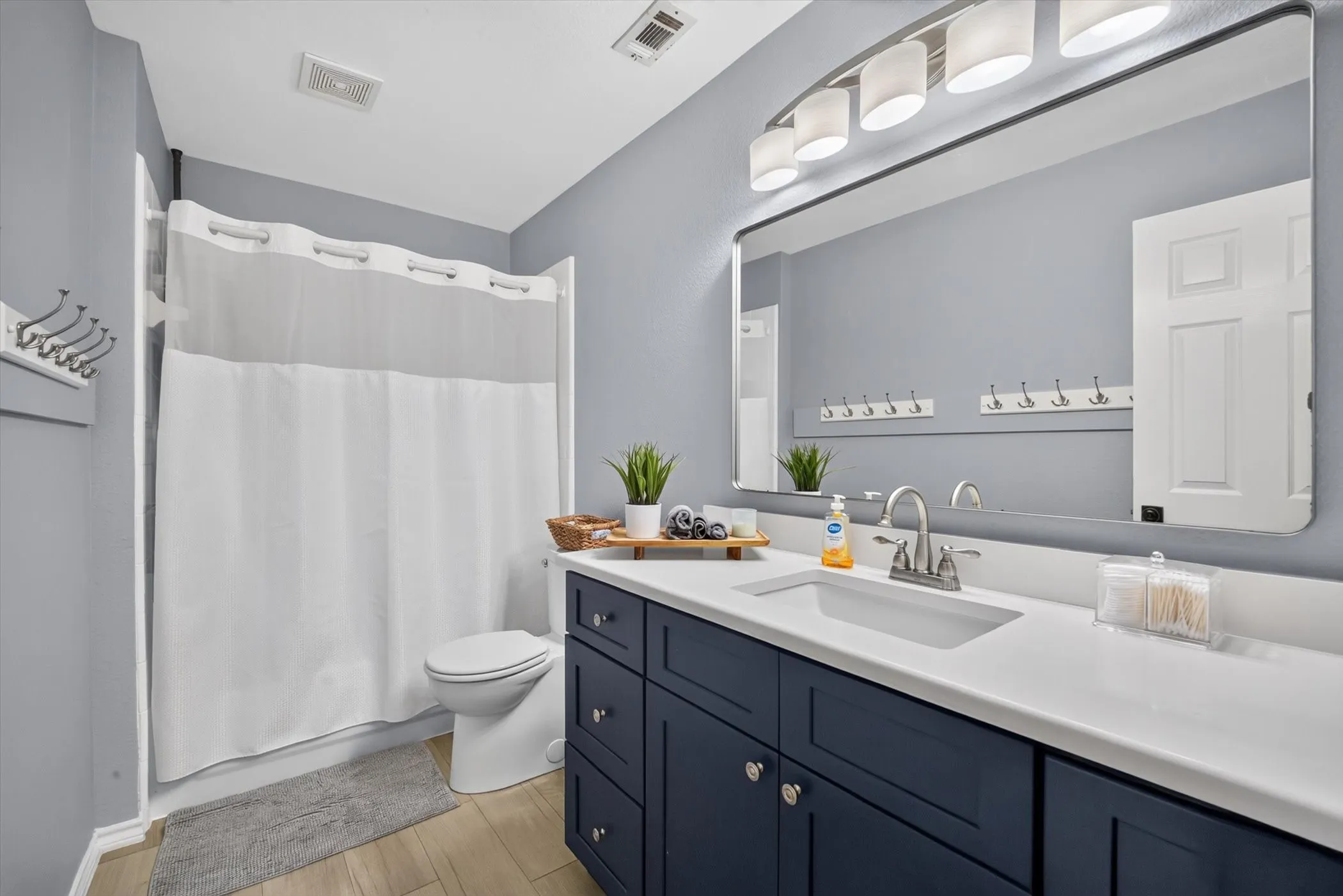 Bathroom featuring a spacious vanity with dark cabinetry and a light-toned countertop, a built-in sink with a chrome faucet, and a large mirror with overhead lighting