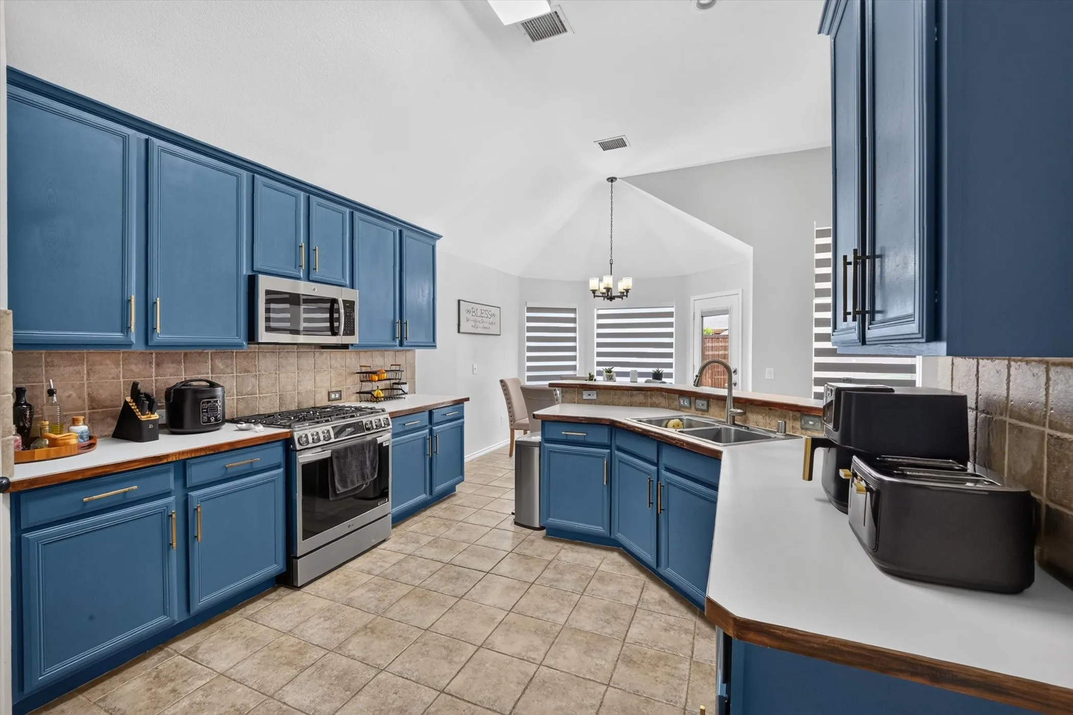 Kitchen featuring blue cabinetry, stainless steel appliances, ceramic tile flooring, and a vaulted ceiling