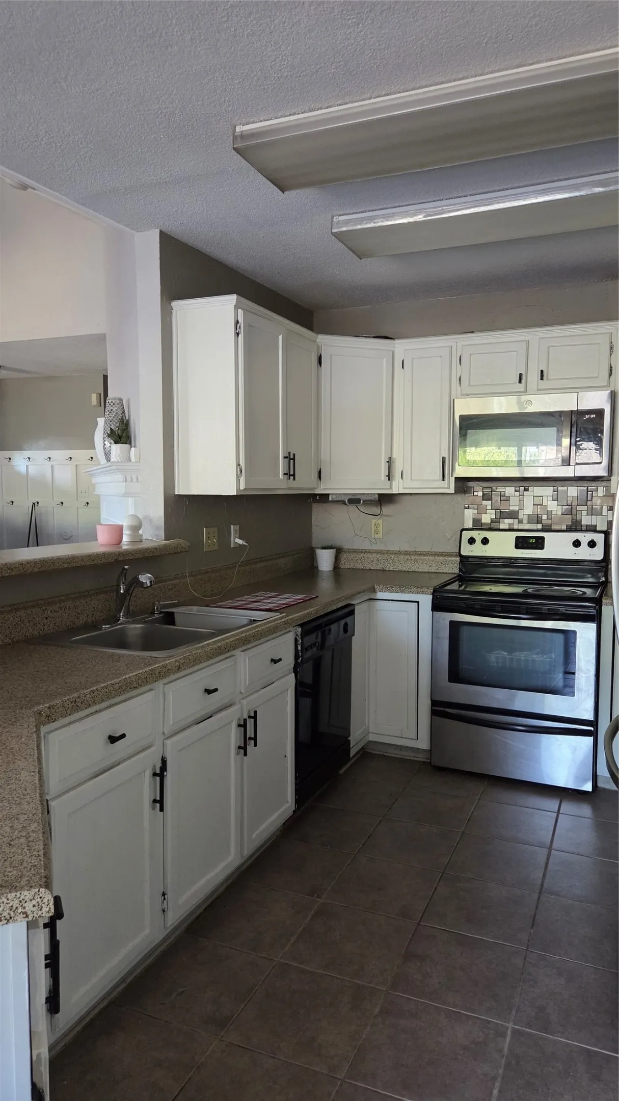 Kitchen featuring white cabinetry with dark hardware, a stainless steel range and microwave, a double basin sink, and tile flooring