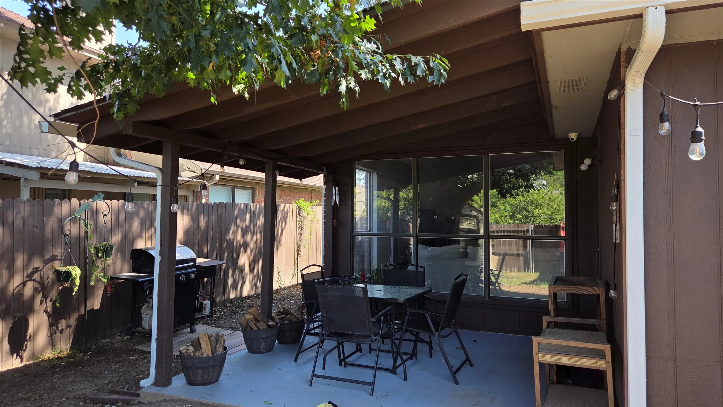 Covered patio with a concrete surface, supported by exposed wood beams, featuring an exterior wall with large windows