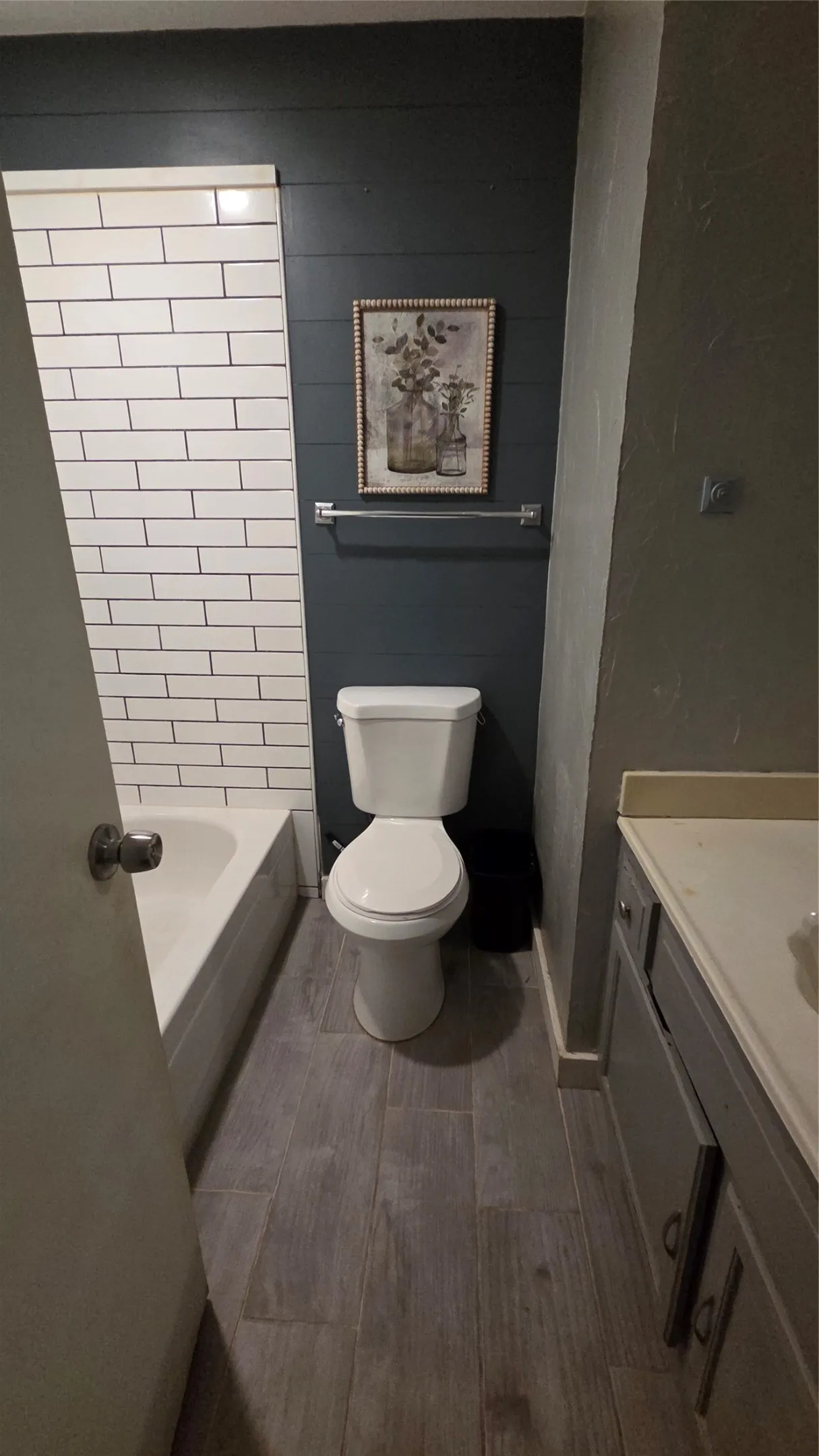 Bathroom featuring a white subway tile surround, plank-style flooring, and a vanity with a light-toned countertop