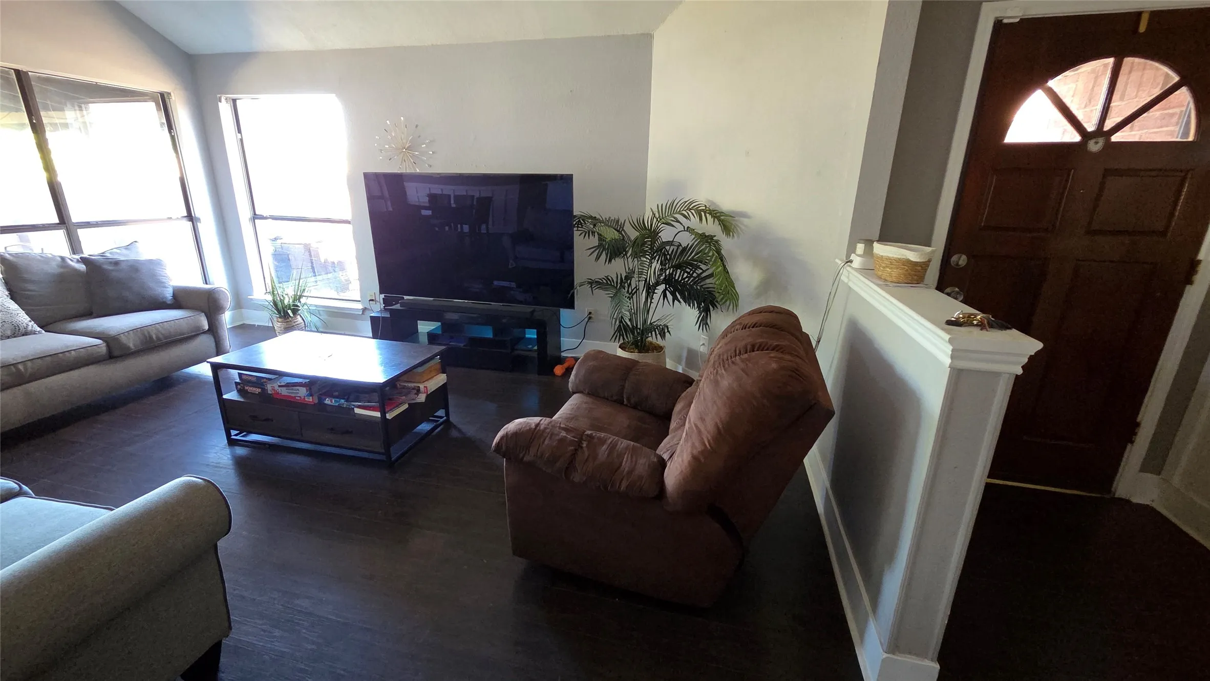 Wood-finish flooring, white wall trim, and a dark wood entry door with an arched glass insert