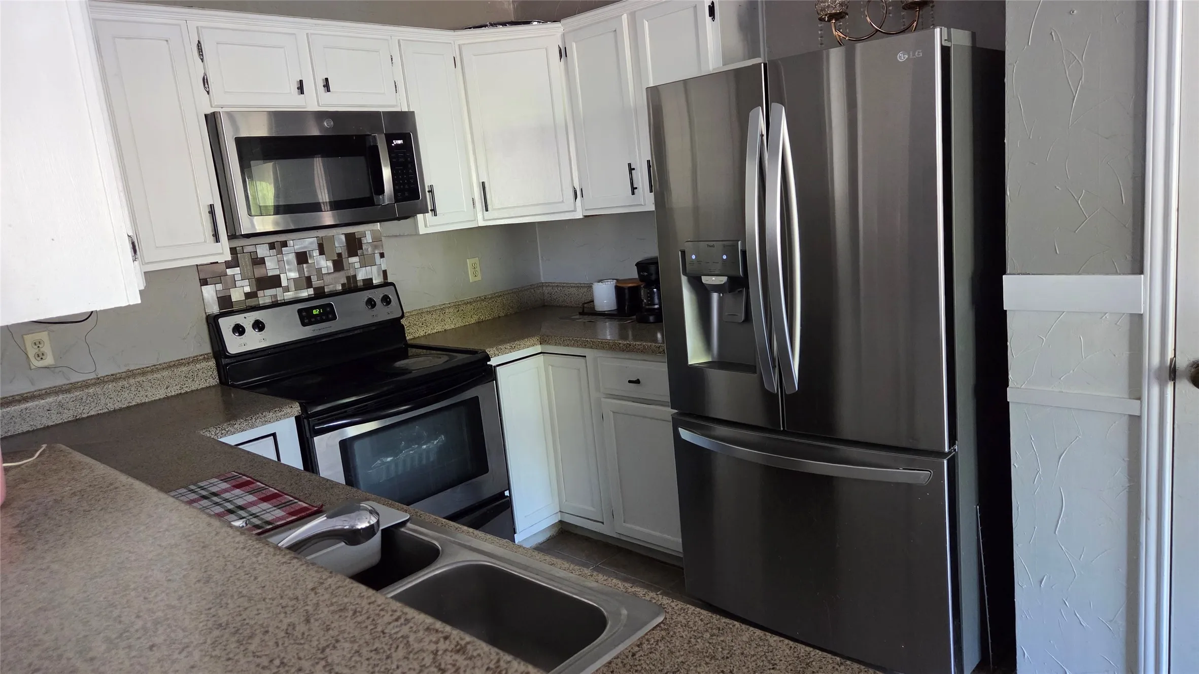 Stainless steel refrigerator, stainless steel microwave, stainless steel range, white cabinetry, and a mosaic tile backsplash