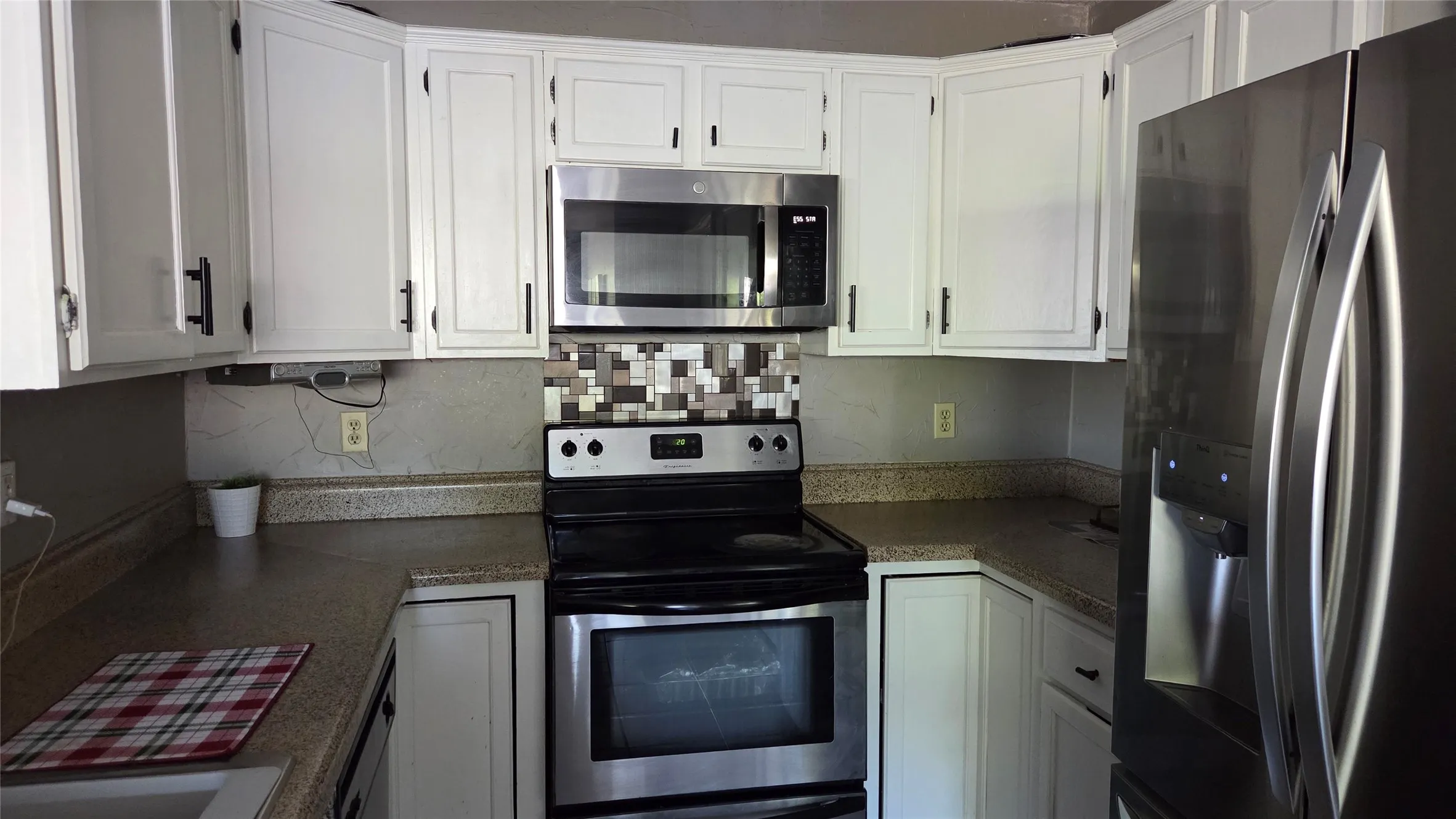 White cabinetry with matte black hardware, stainless steel appliances, speckled countertops, and a mosaic tile backsplash