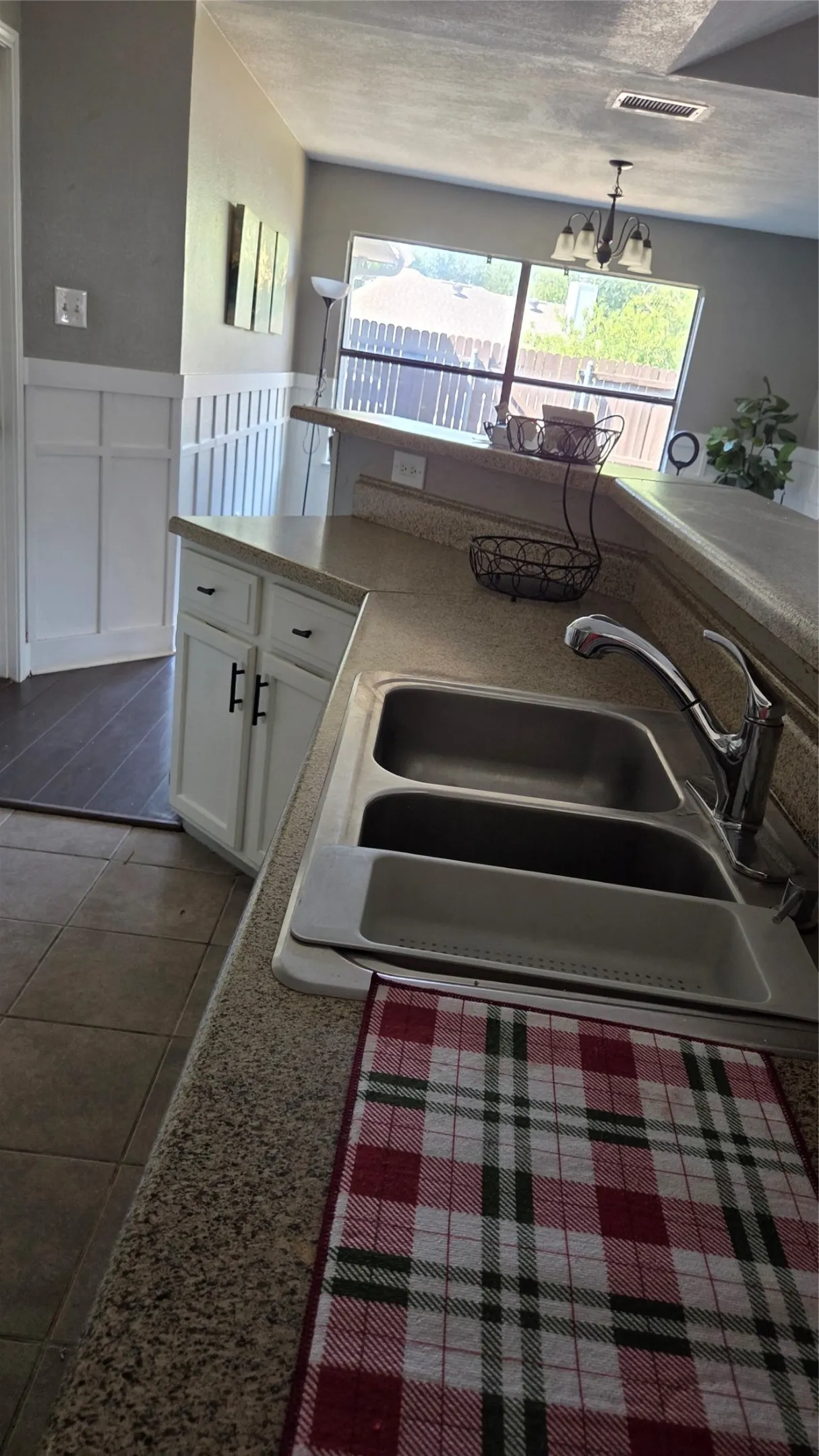 Kitchen featuring a double stainless steel sink, speckled countertop, white cabinetry with dark hardware, and a window overlooking the outdoor area