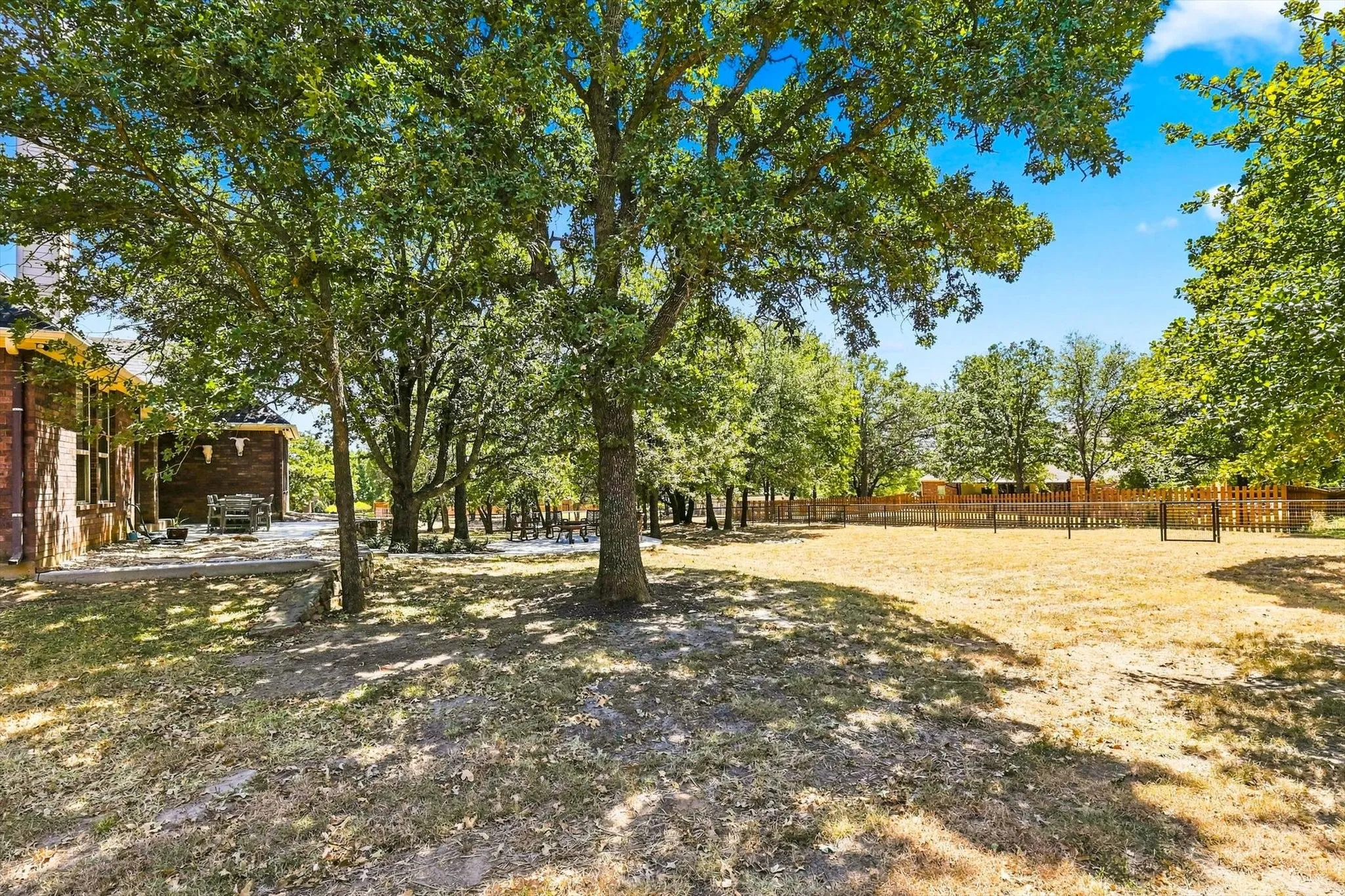 Expansive outdoor area featuring mature trees, a brick exterior, and a wood fence
