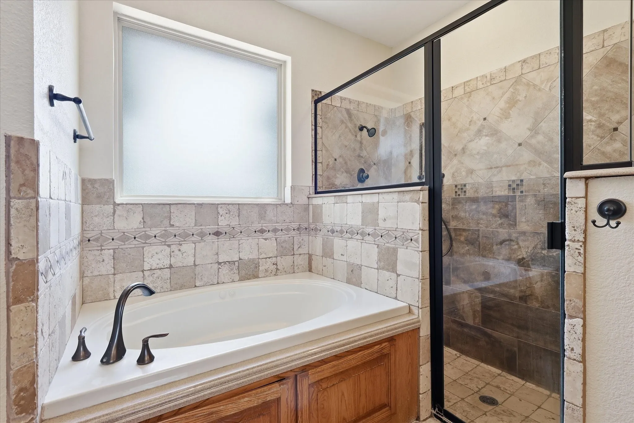Built-in soaking tub with bronze-finish fixtures, tile surround with decorative accent band, and a frosted window