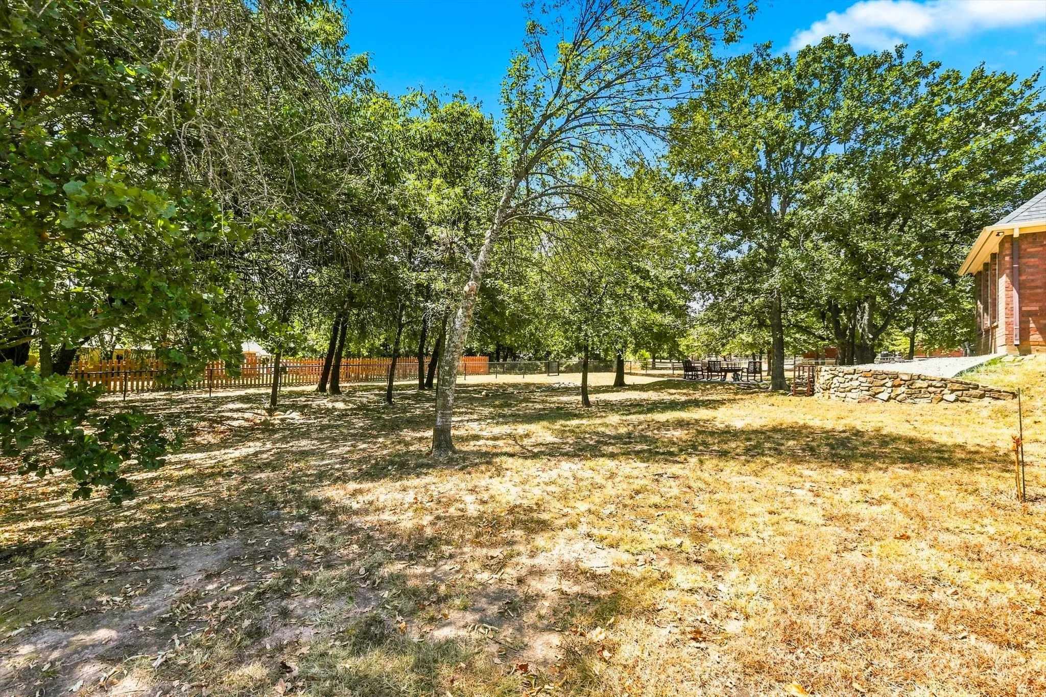 Expansive outdoor space featuring mature trees, a wooden fence, and a stone retaining wall