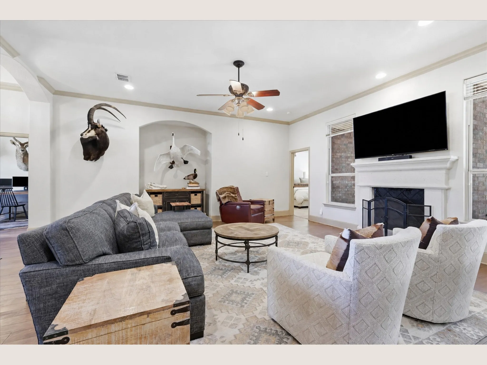 Spacious living area featuring a fireplace with a white mantel, wood-finish flooring, recessed lighting, and a ceiling fan