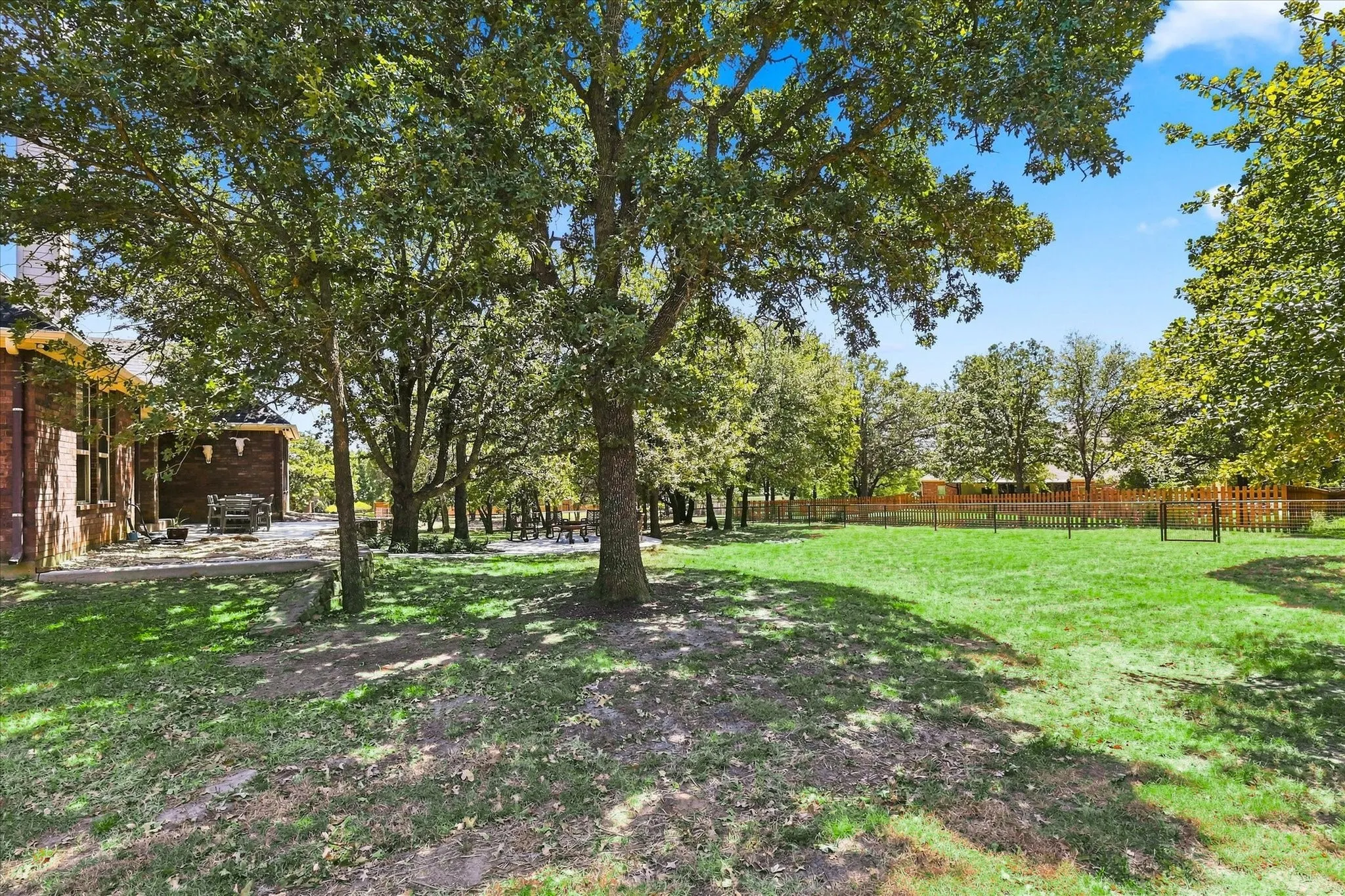 Expansive green space featuring mature trees, a wood privacy fence, and brick exterior