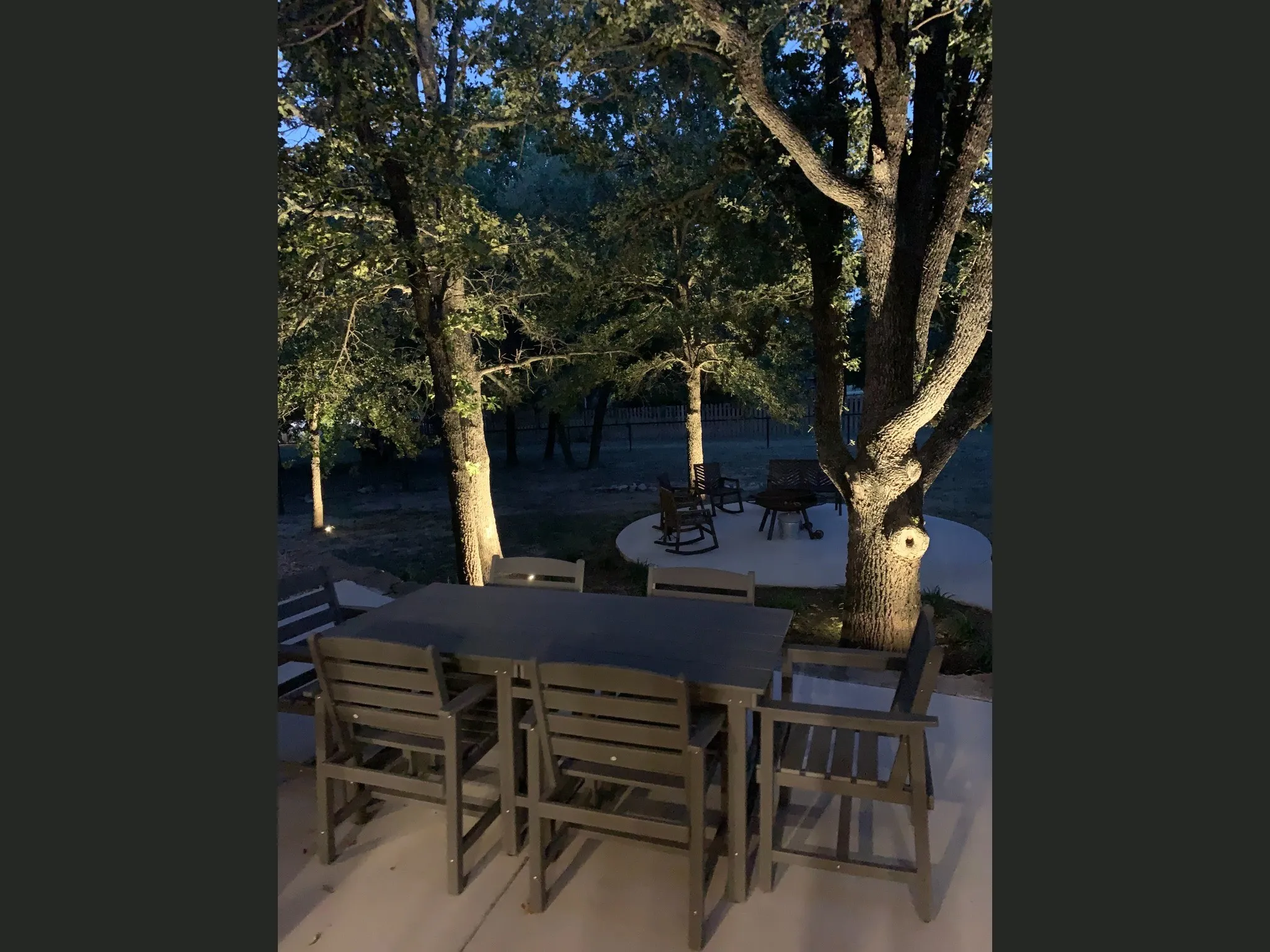 Patio area with concrete surfacing, surrounded by mature trees, and featuring integrated landscape lighting