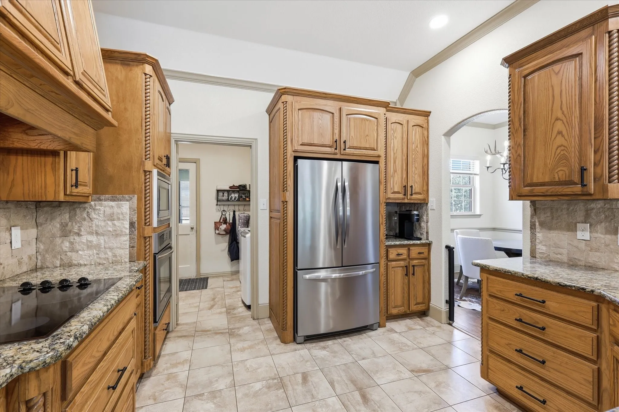 Gourmet kitchen featuring wood cabinetry, stainless steel appliances, stone countertops, and a tiled backsplash