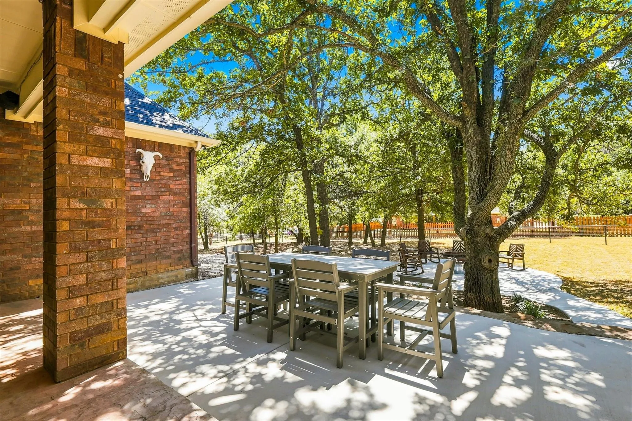 Exterior patio featuring a concrete surface, a brick column, and mature trees providing natural shade