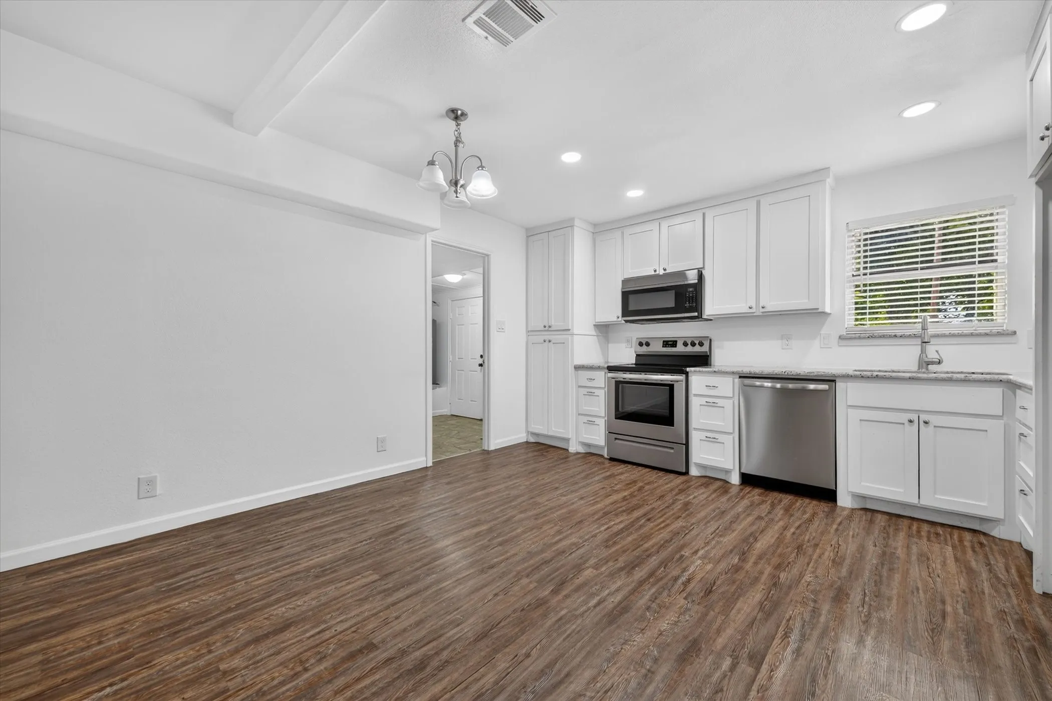 Kitchen with white cabinetry, stainless steel appliances, and wood-finish flooring