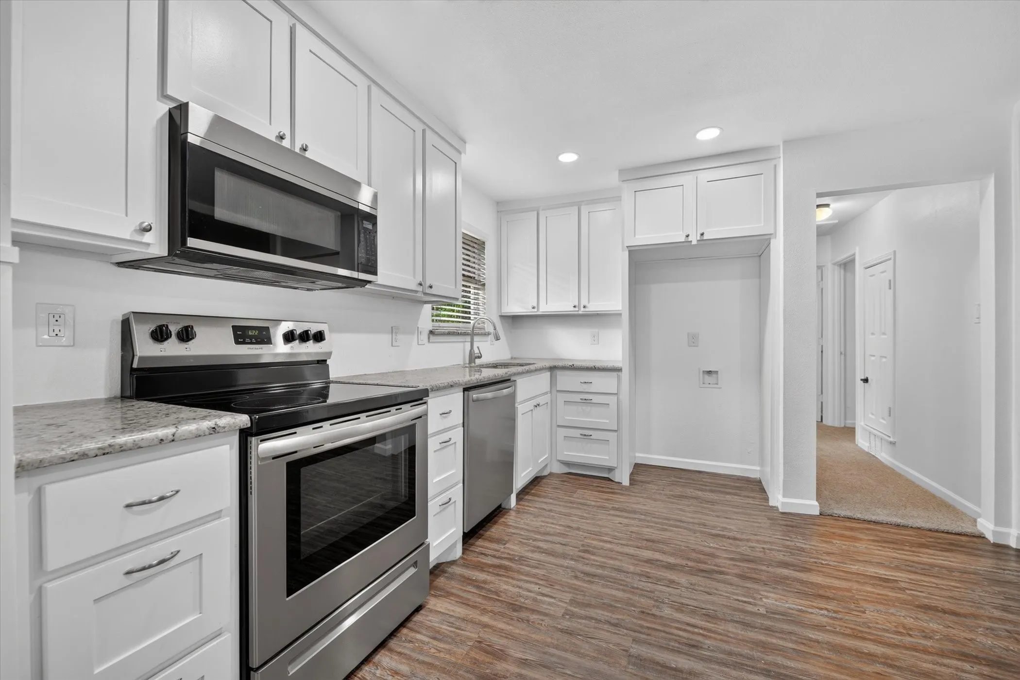 Kitchen featuring white shaker-style cabinetry, stainless steel appliances, granite countertops, and wood-finish flooring