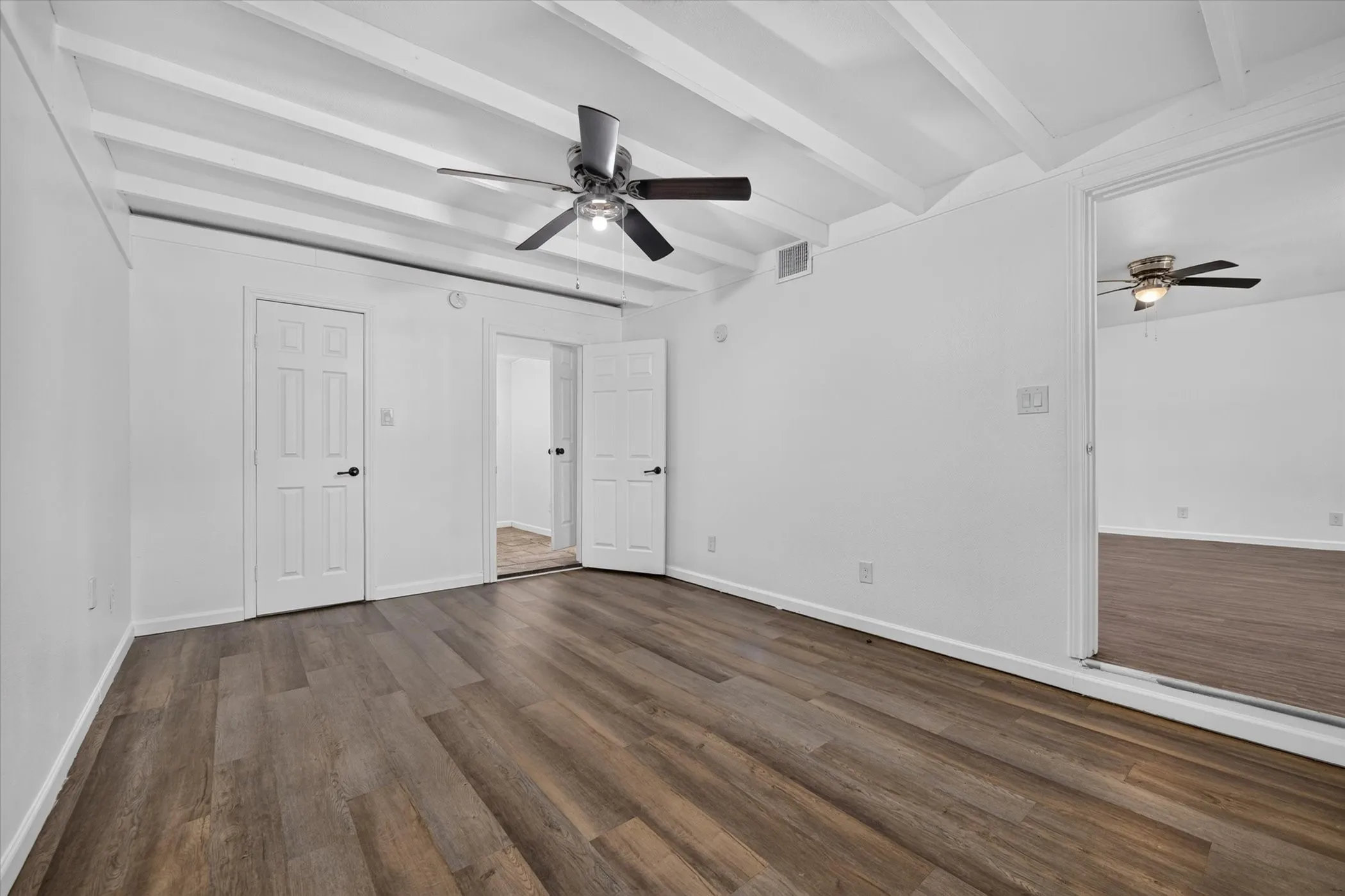 Wood-finish flooring, white walls, exposed white ceiling beams, ceiling fan, and sliding mirrored doors