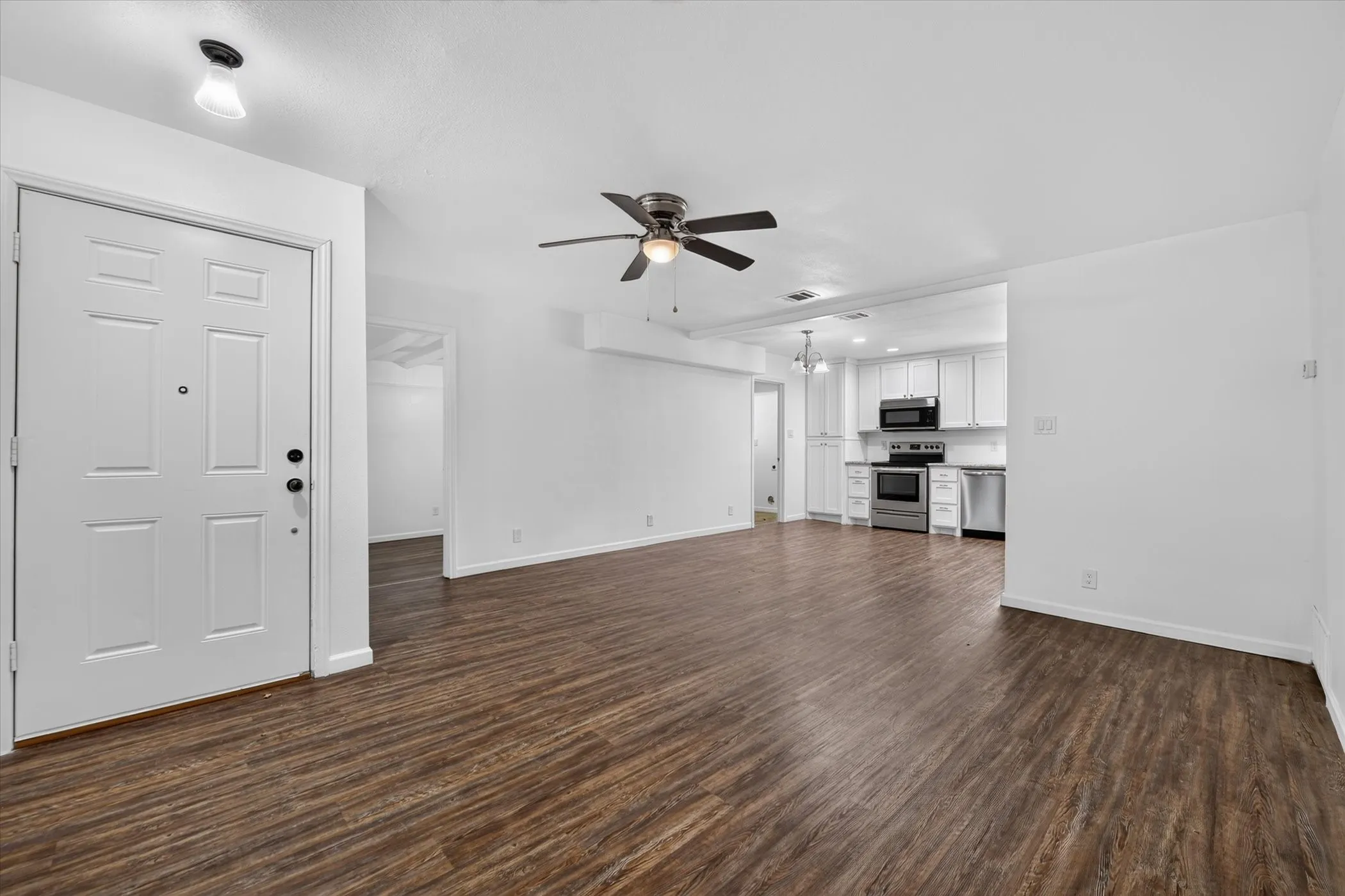 Wood-finish flooring, ceiling fan, white paneled entry door, white cabinetry, and stainless steel appliances