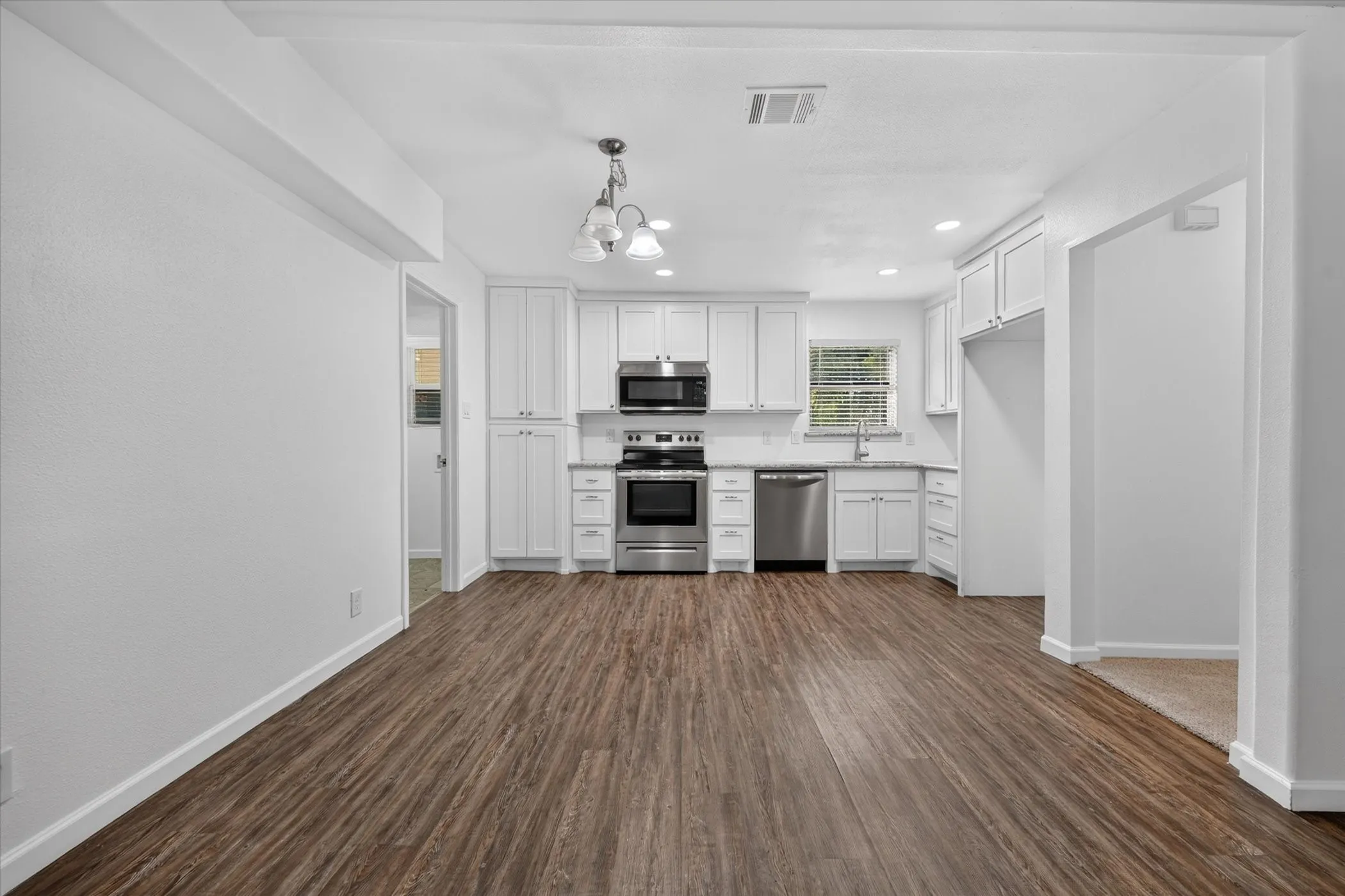 White shaker cabinetry with stainless steel appliances, wood-finish flooring, and light-colored countertops