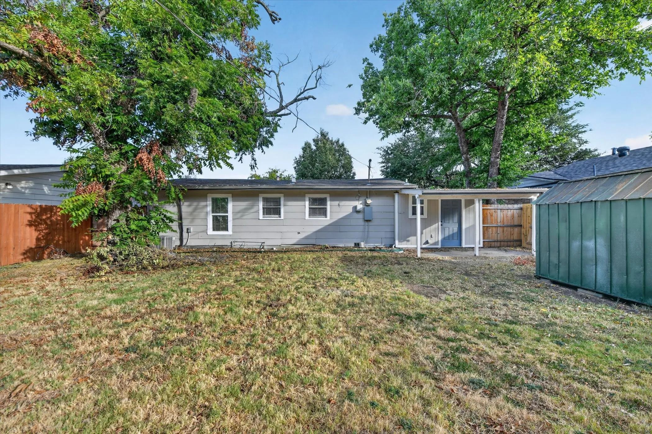 Expansive backyard with a covered patio, privacy fencing, and a detached storage shed