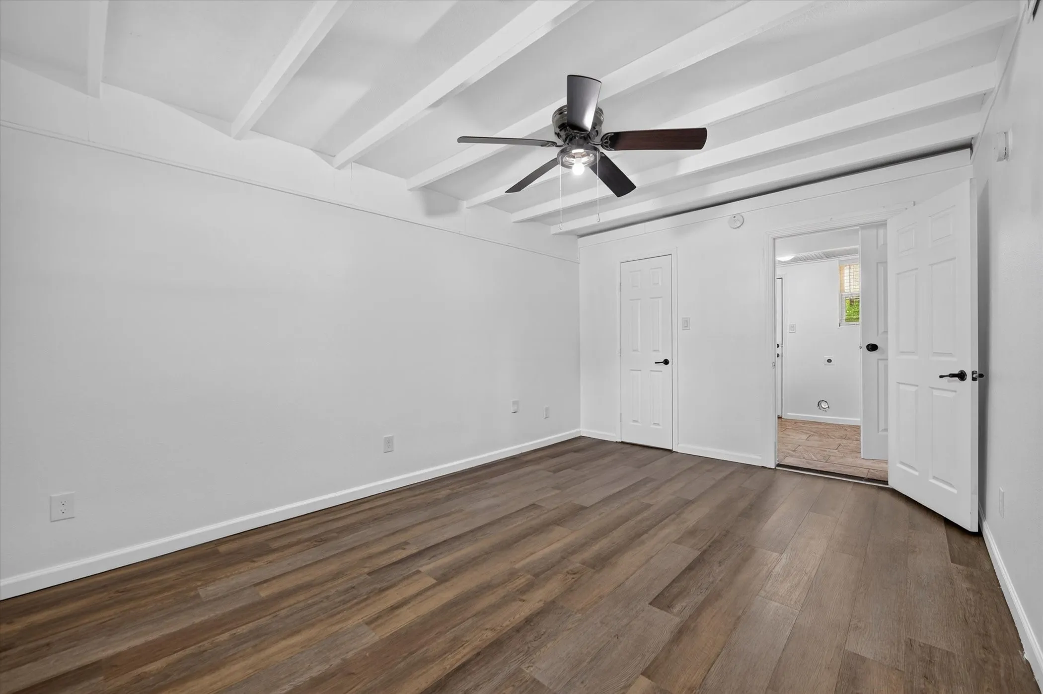 Exposed beam ceiling with a ceiling fan, wood-finish flooring, and white interior doors with dark hardware