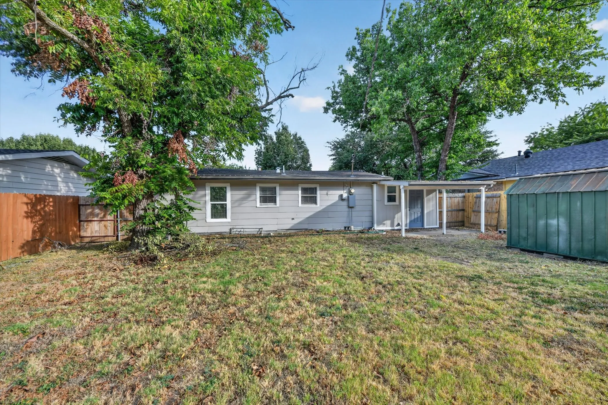 Expansive backyard with a covered patio, established trees, and a storage shed