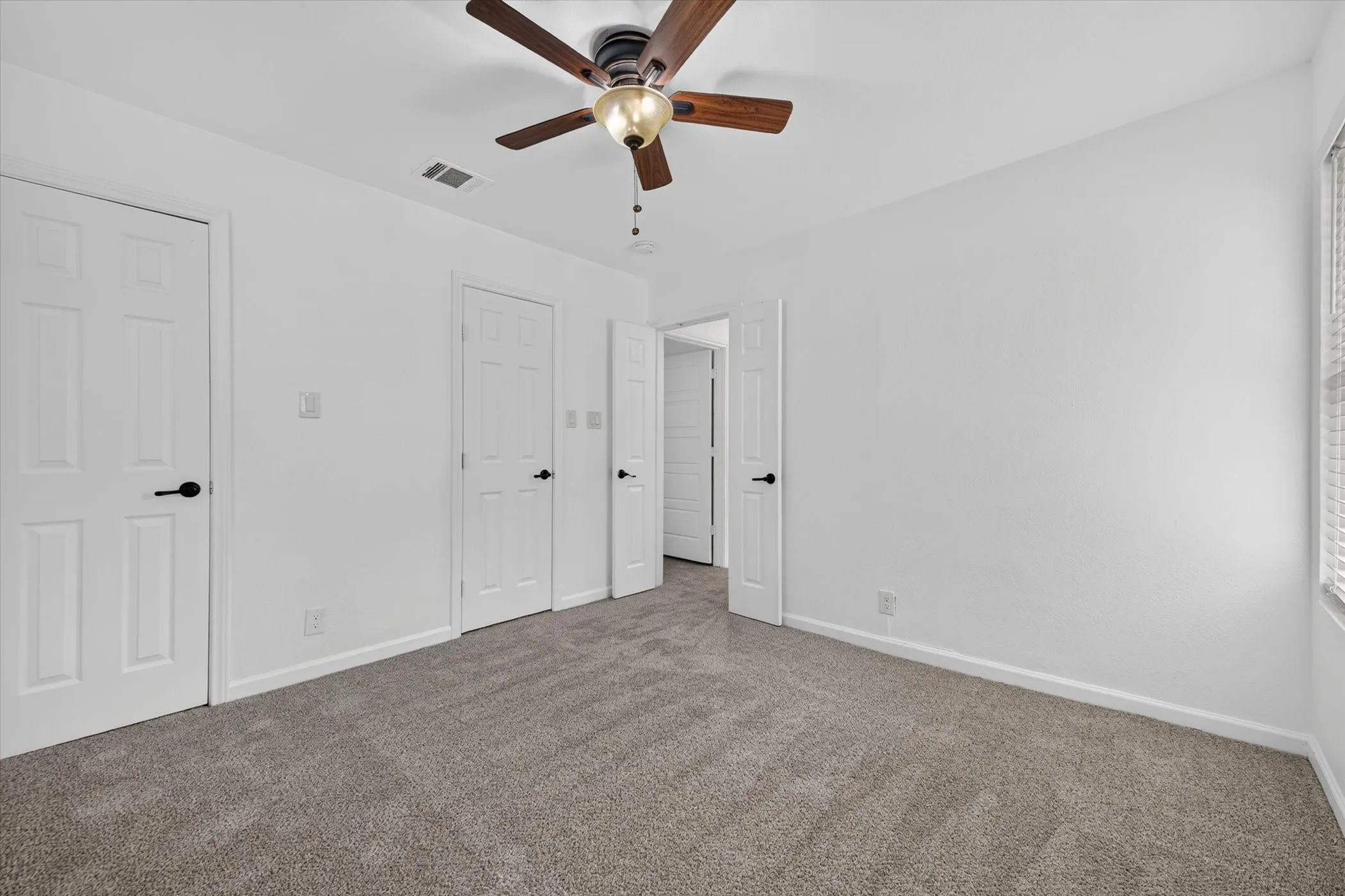 White paneled doors with black hardware, wood-finish ceiling fan, and grey carpeted flooring