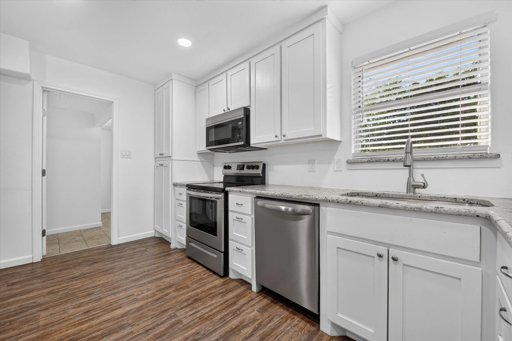 White shaker cabinetry, stainless steel appliances, wood-finish flooring, light-toned countertops, and a stainless steel sink with a gooseneck faucet