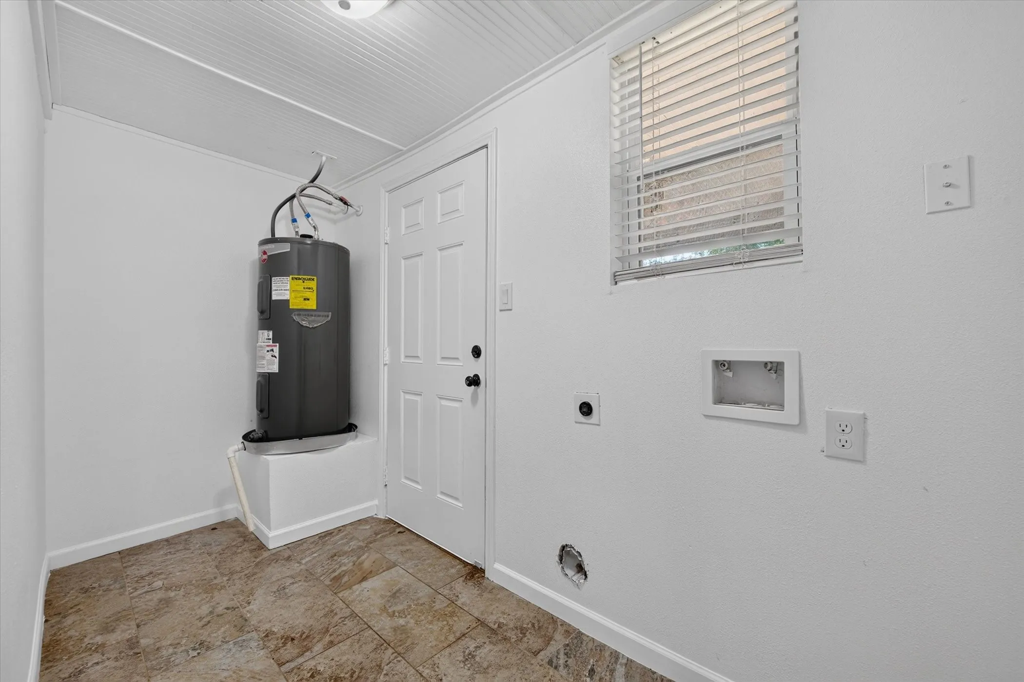 Utility space featuring a water heater, patterned tile flooring, and a white paneled door
