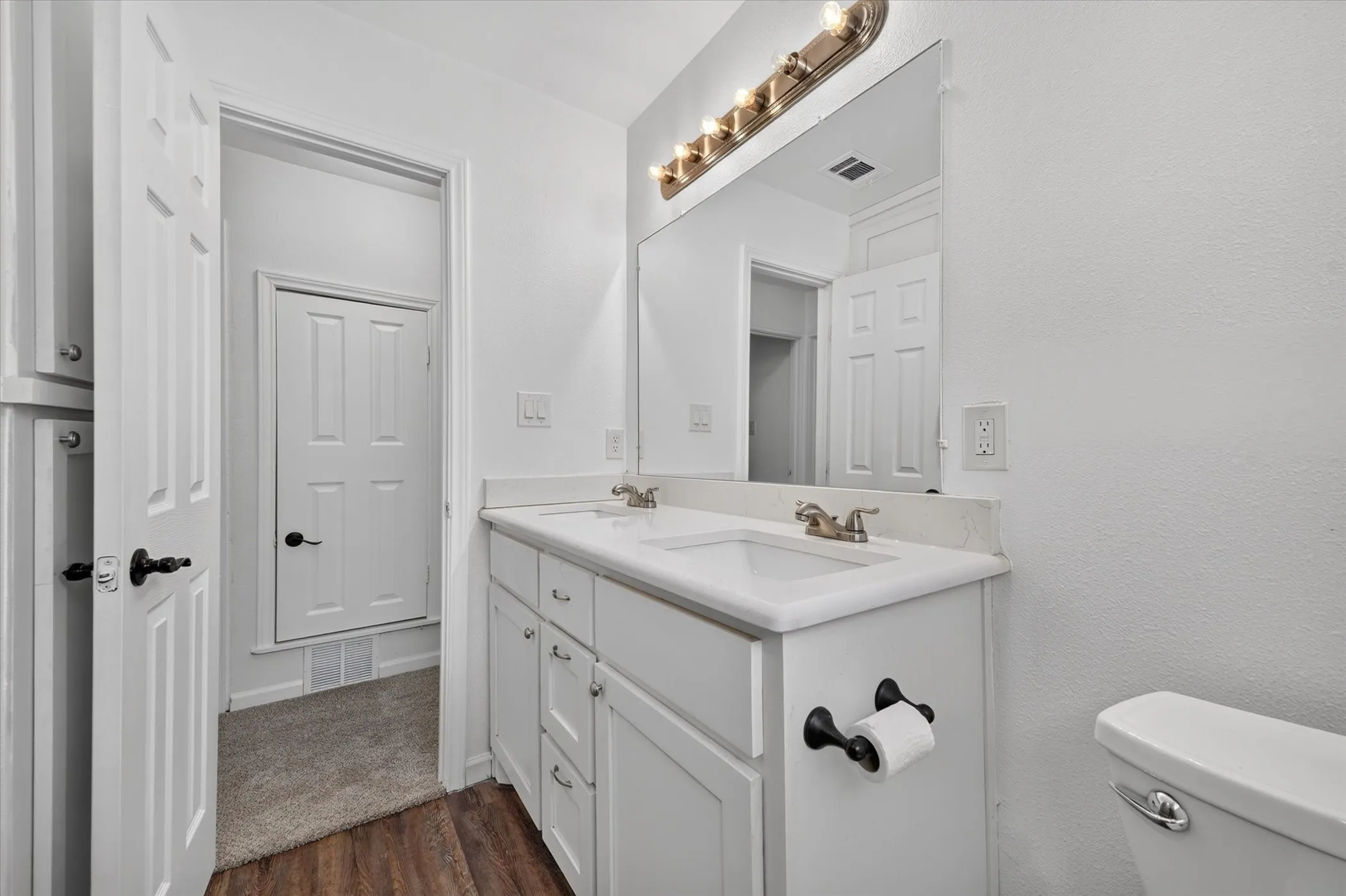 Double vanity with integrated sinks, white cabinetry, wall-mounted lighting, and wood-finish flooring