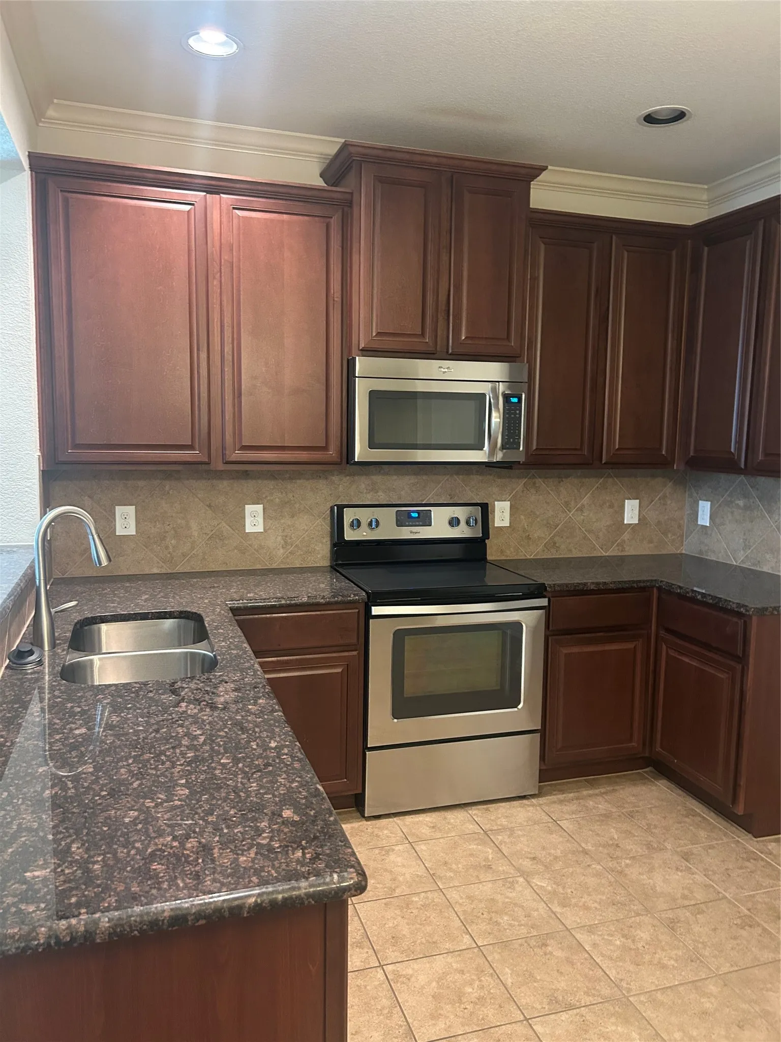 Kitchen featuring wood-finish cabinetry, stainless steel appliances, a double basin sink, granite countertops, and tile flooring