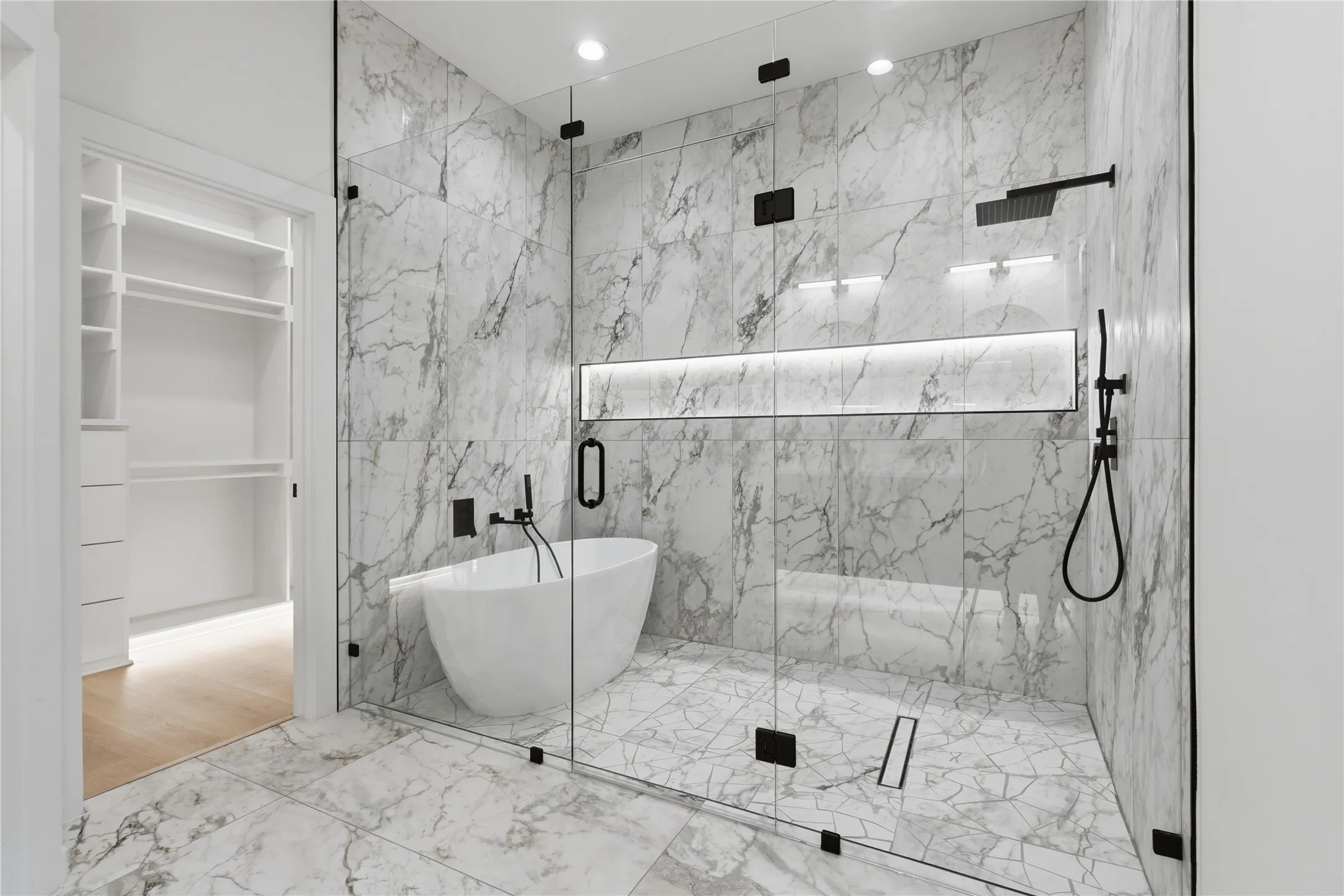 Glass-enclosed shower with a freestanding soaking tub, marble-finish tile, and matte black fixtures