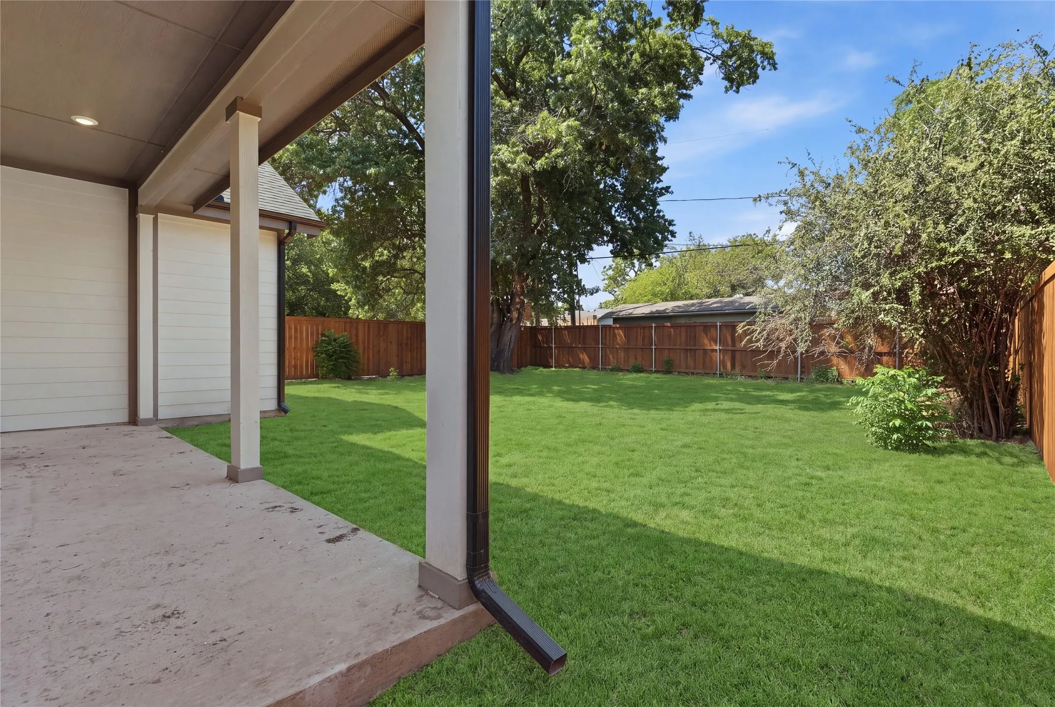 Expansive green lawn with a wooden perimeter fence, covered patio, and recessed lighting