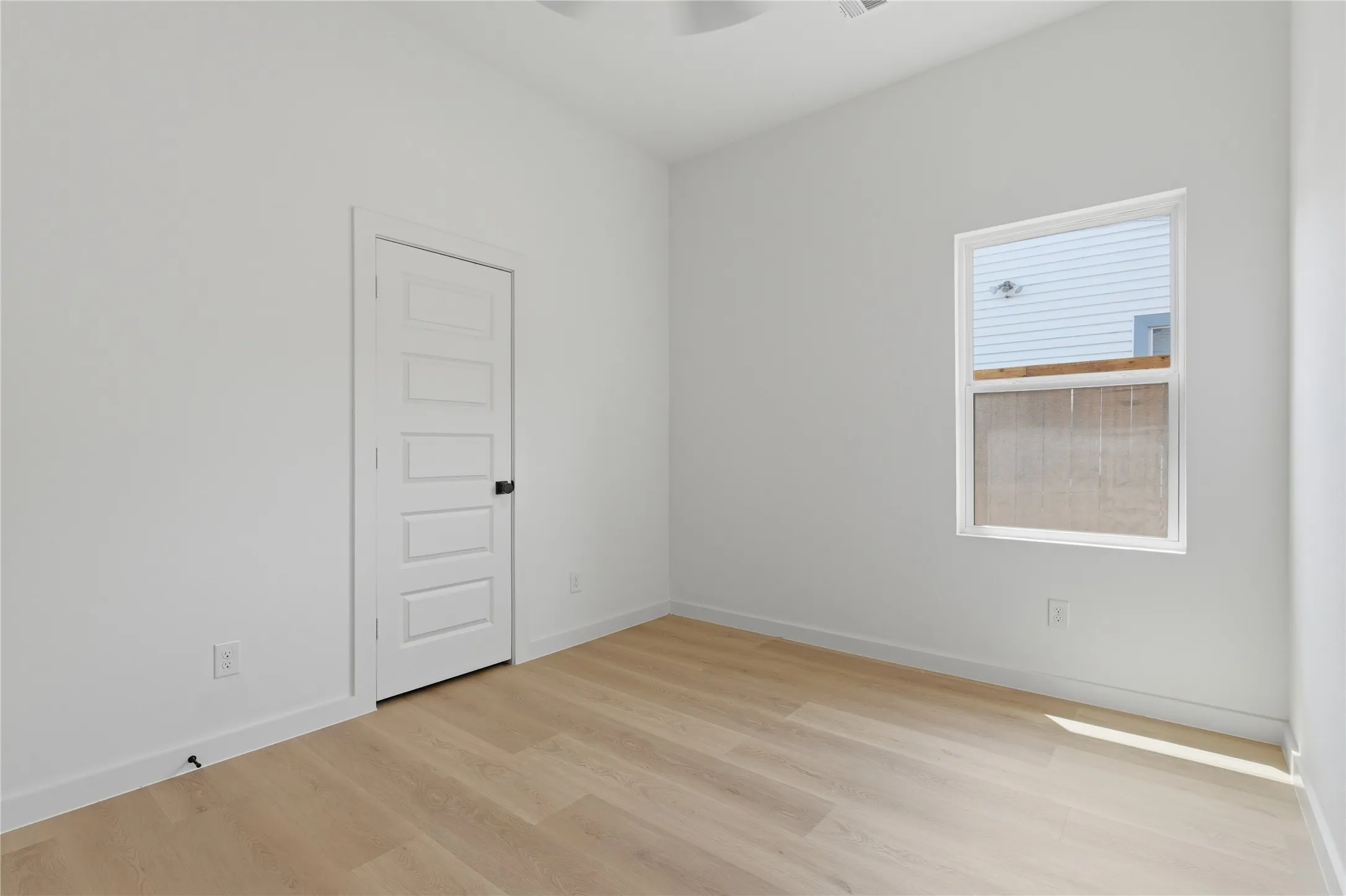 Wood-finish flooring, white walls, five-panel door with black hardware, and a single pane window