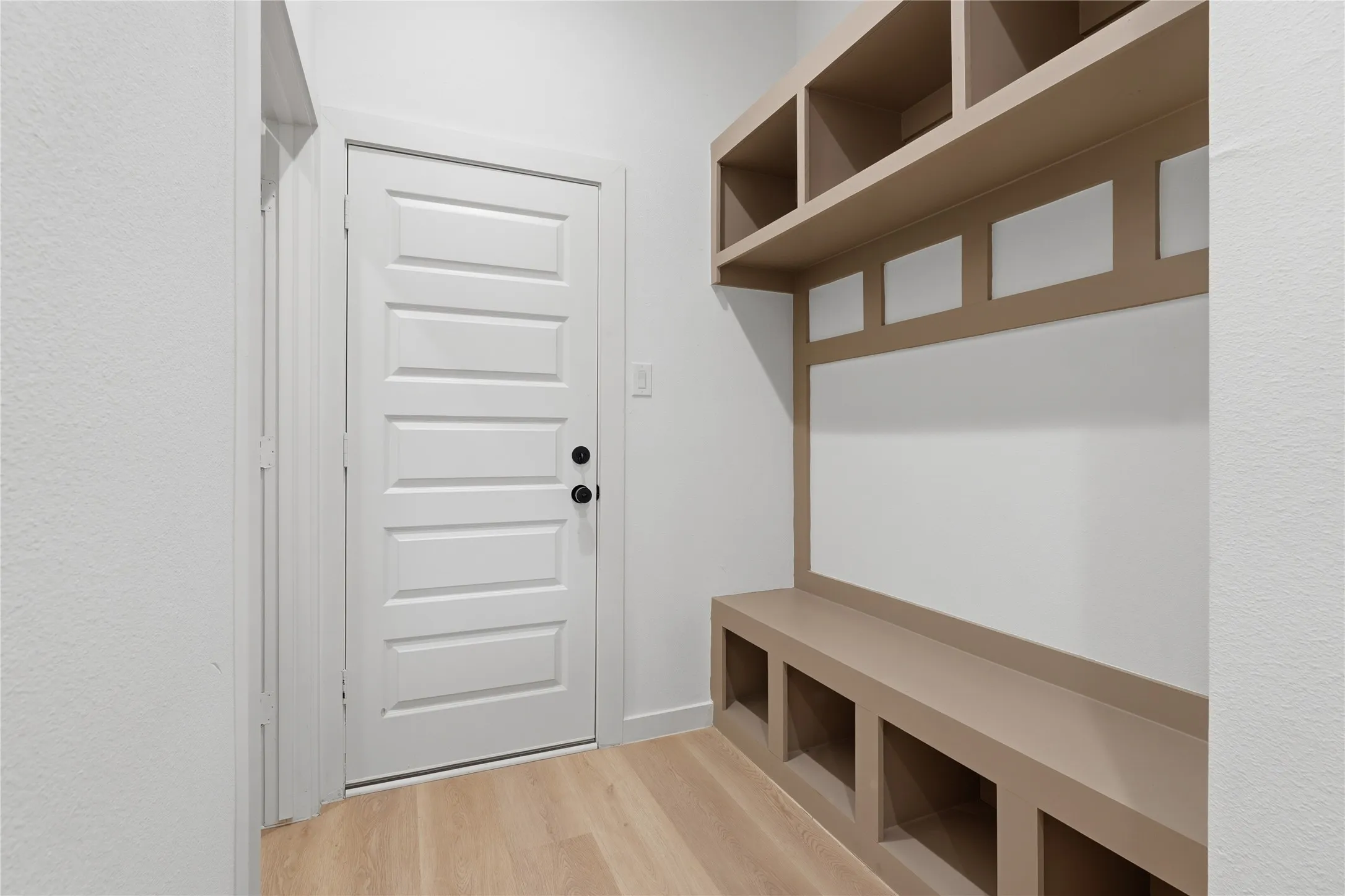 Built-in storage bench with open cubbies, integrated shelving, wood-finish flooring, and a paneled interior door